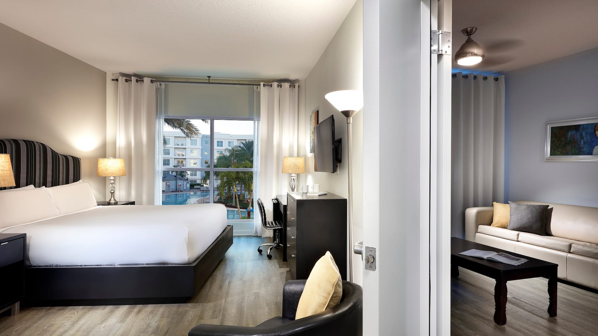 Modern hotel suite with king bed, pool view, and adjoining living room.