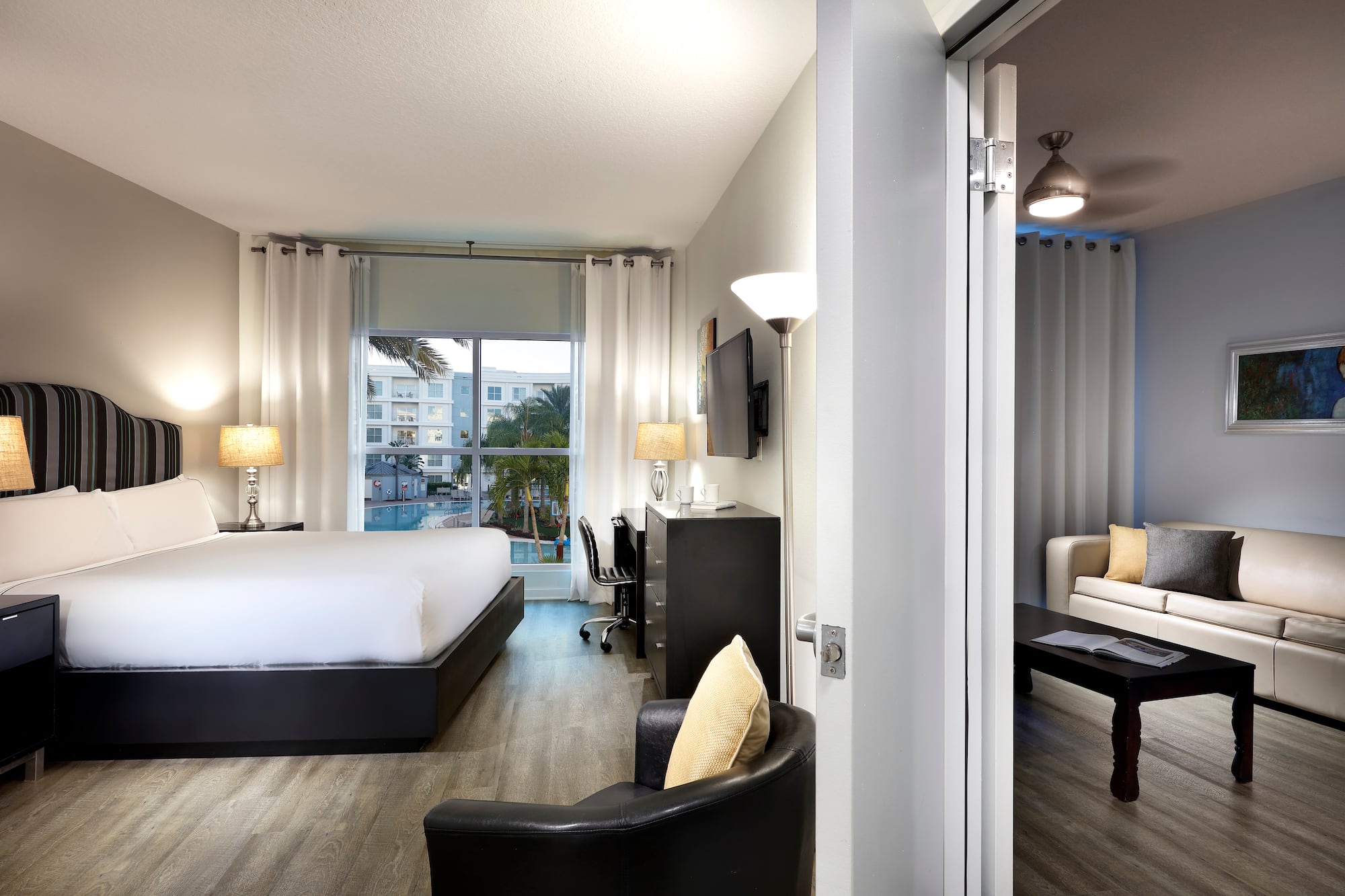 Modern hotel suite with king bed, pool view, and adjoining living room.