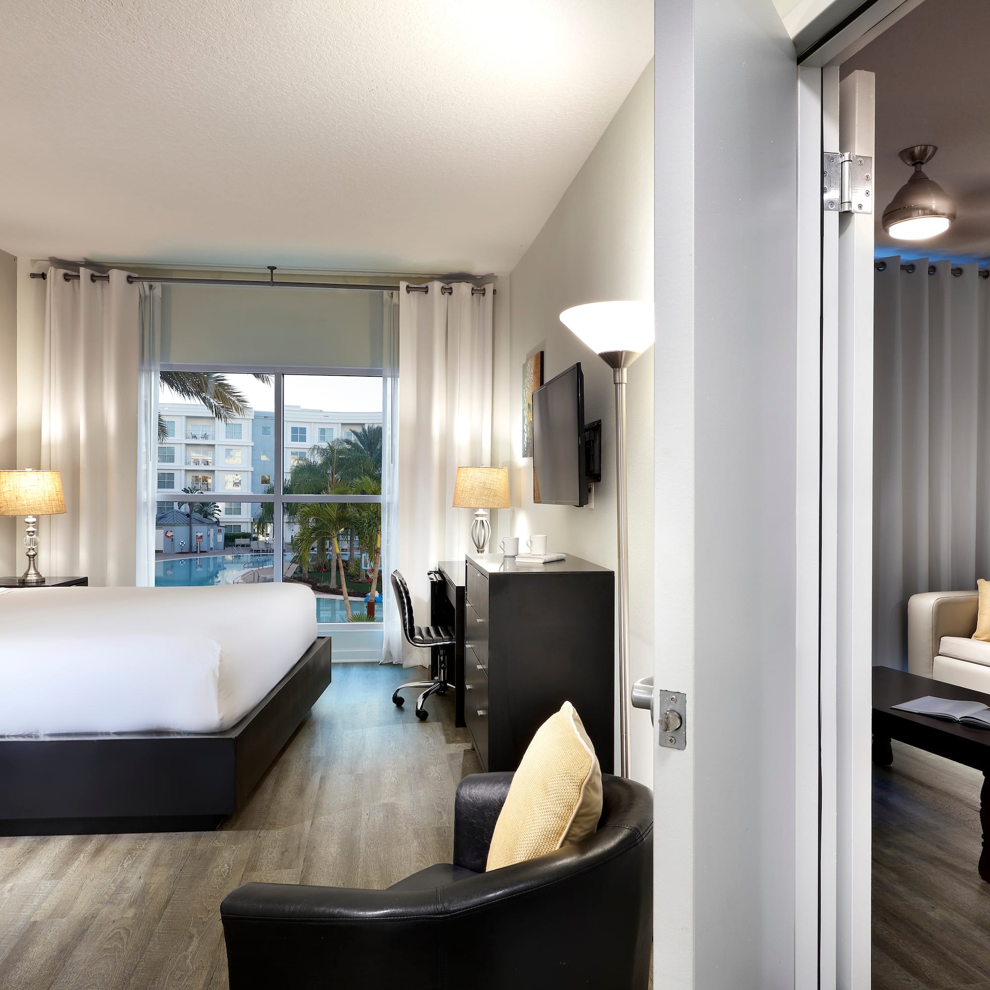 Modern hotel suite with king bed, pool view, and adjoining living room.