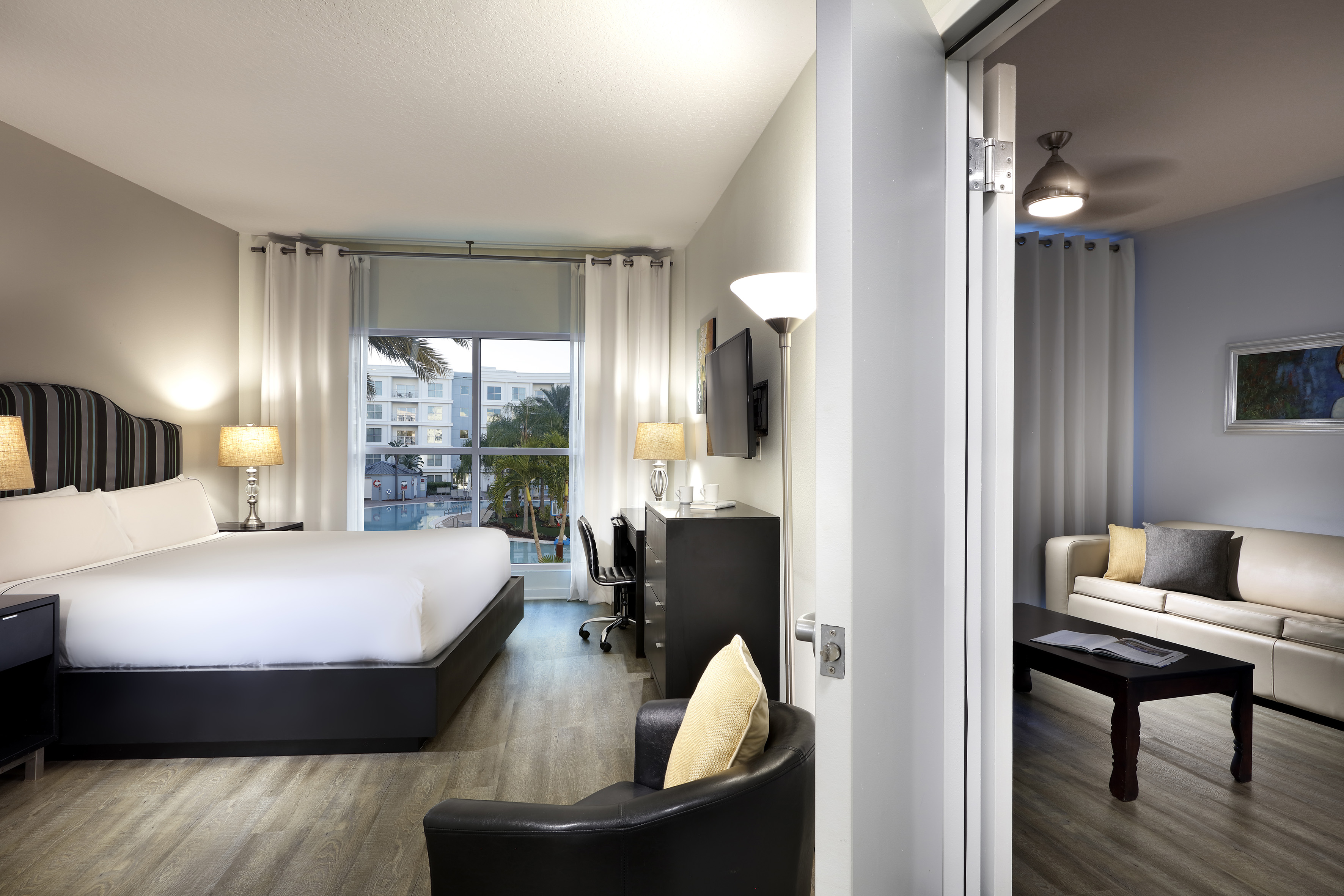 Modern hotel suite with king bed, pool view, and adjoining living room.