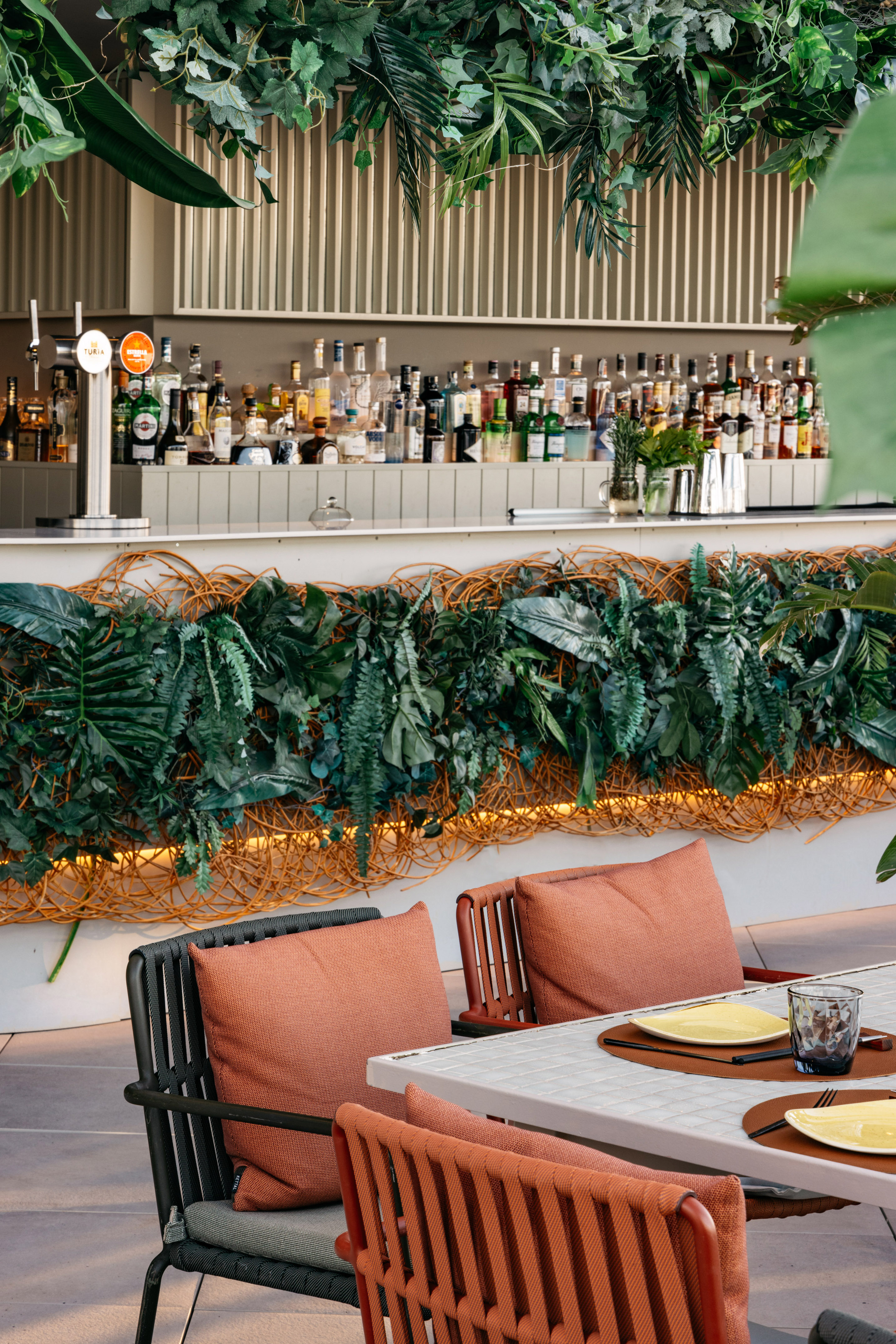 Tropical bar decor with lush greenery, liquor bottles, and outdoor dining tables.