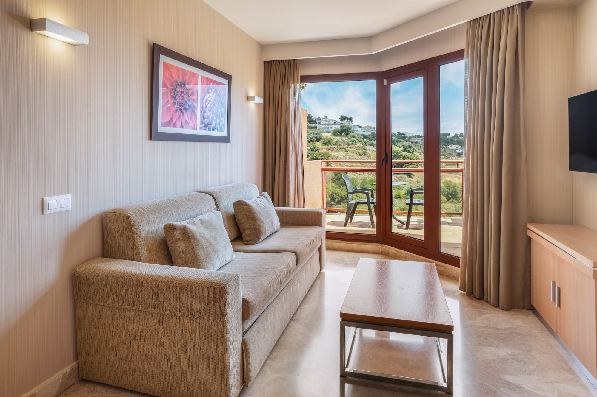 Hotel suite living room with sofa, balcony, and panoramic hill views.