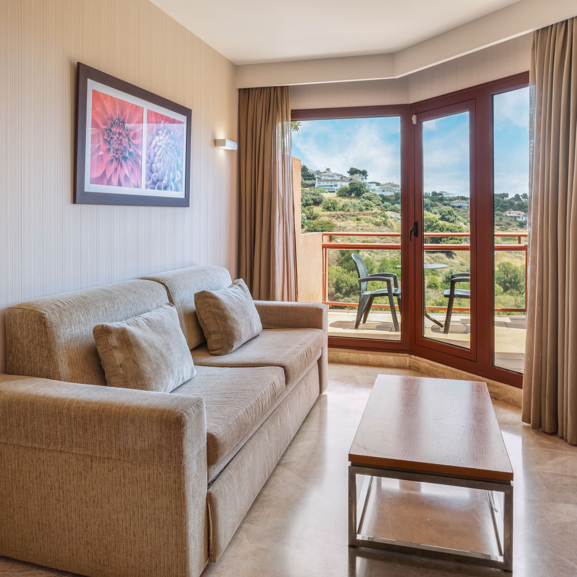 Modern living room with beige sofa, coffee table, and balcony overlooking hills.