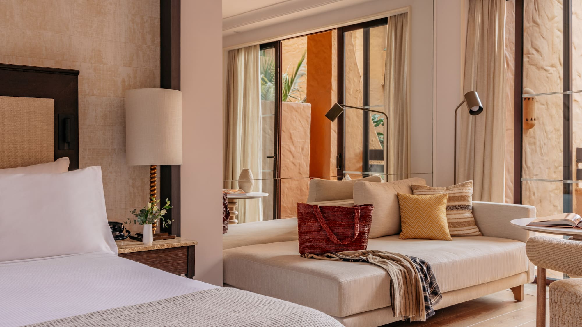 Modern resort suite with bed, daybed, and warm terracotta patio view.