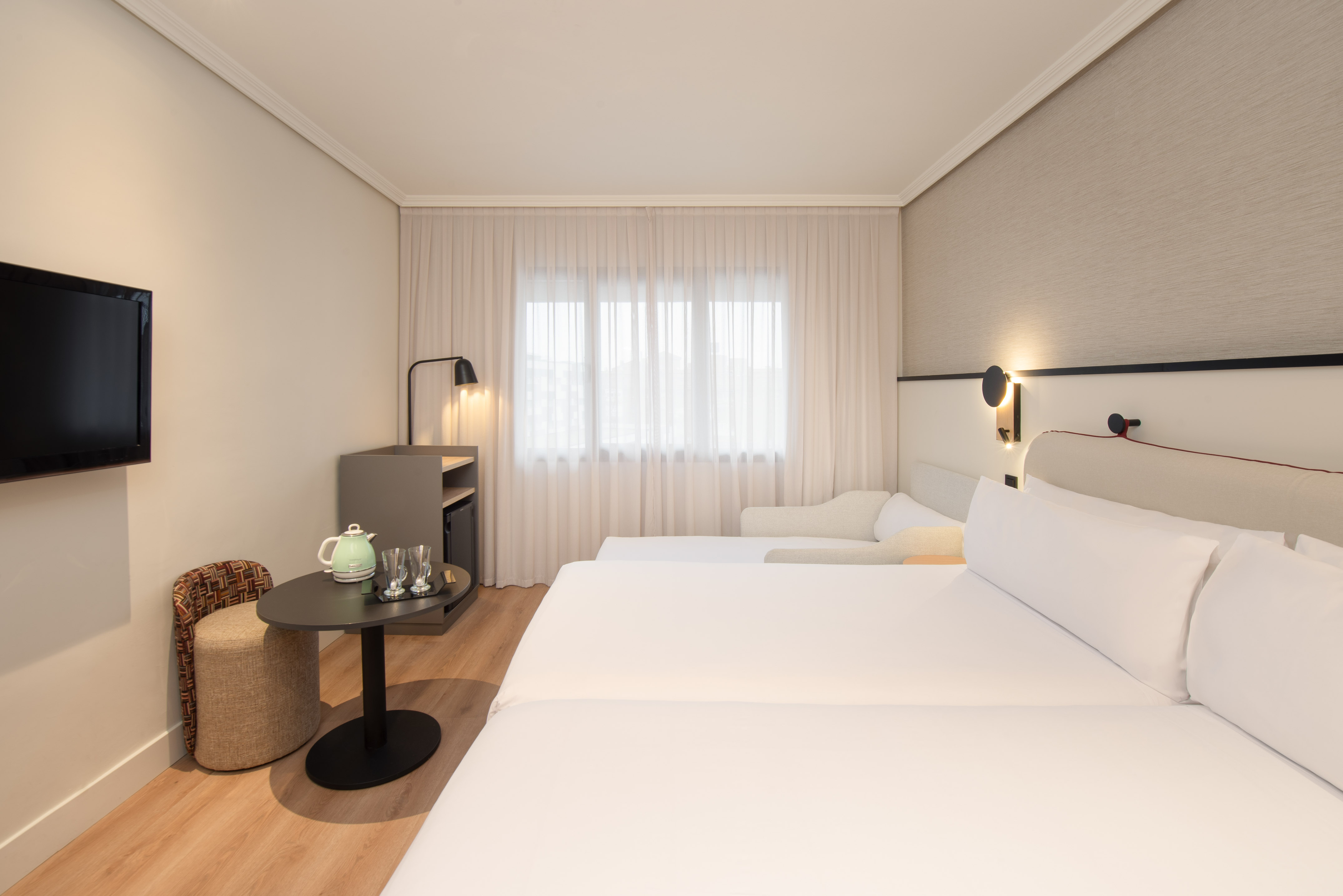 Bright hotel guest room with twin beds, TV, kettle, and modern decor.