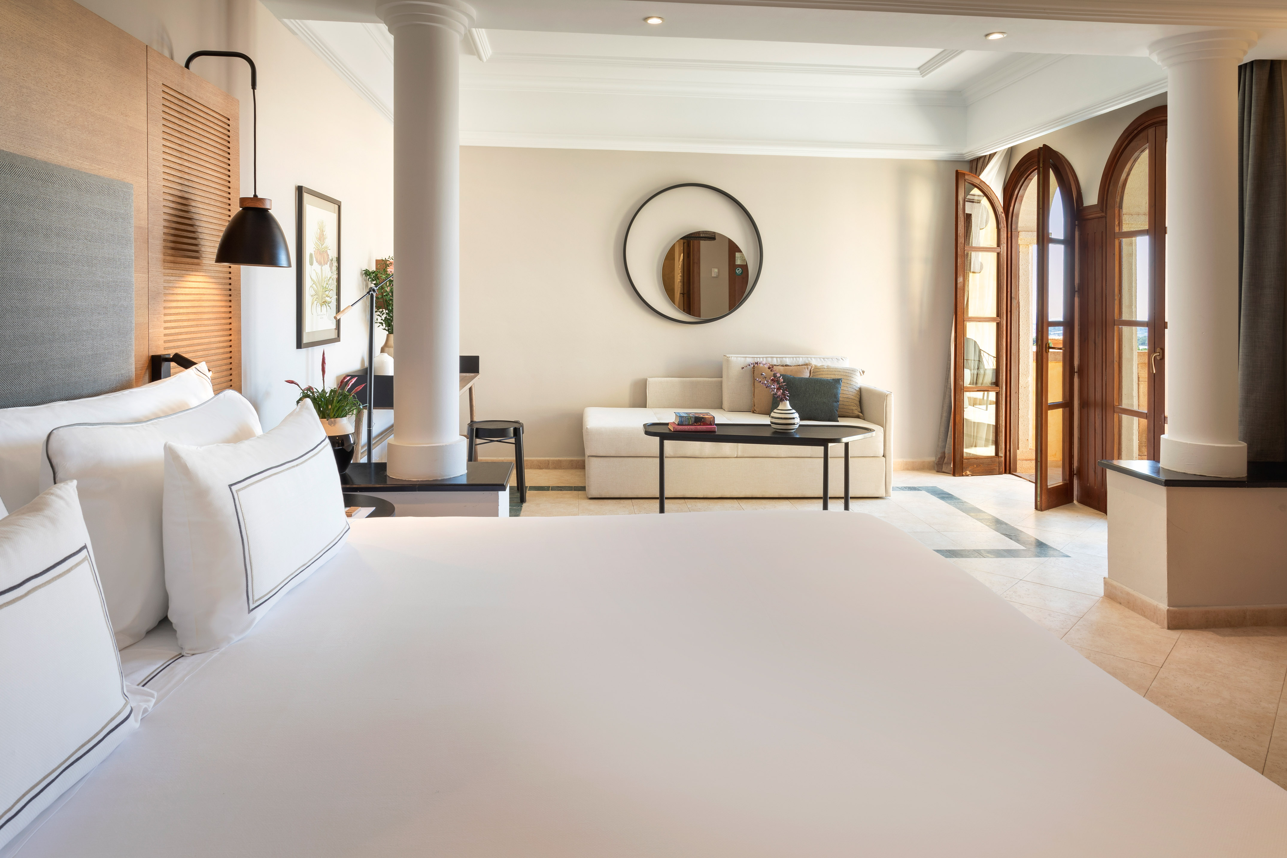 Modern hotel room with large bed, sofa, and arched balcony doors.