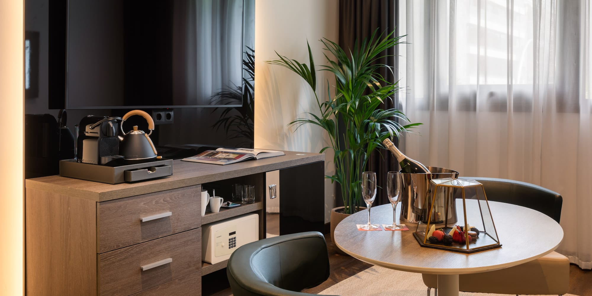 Habitación de hotel moderna con TV, cafetera, champagne, mesa y minibar.
