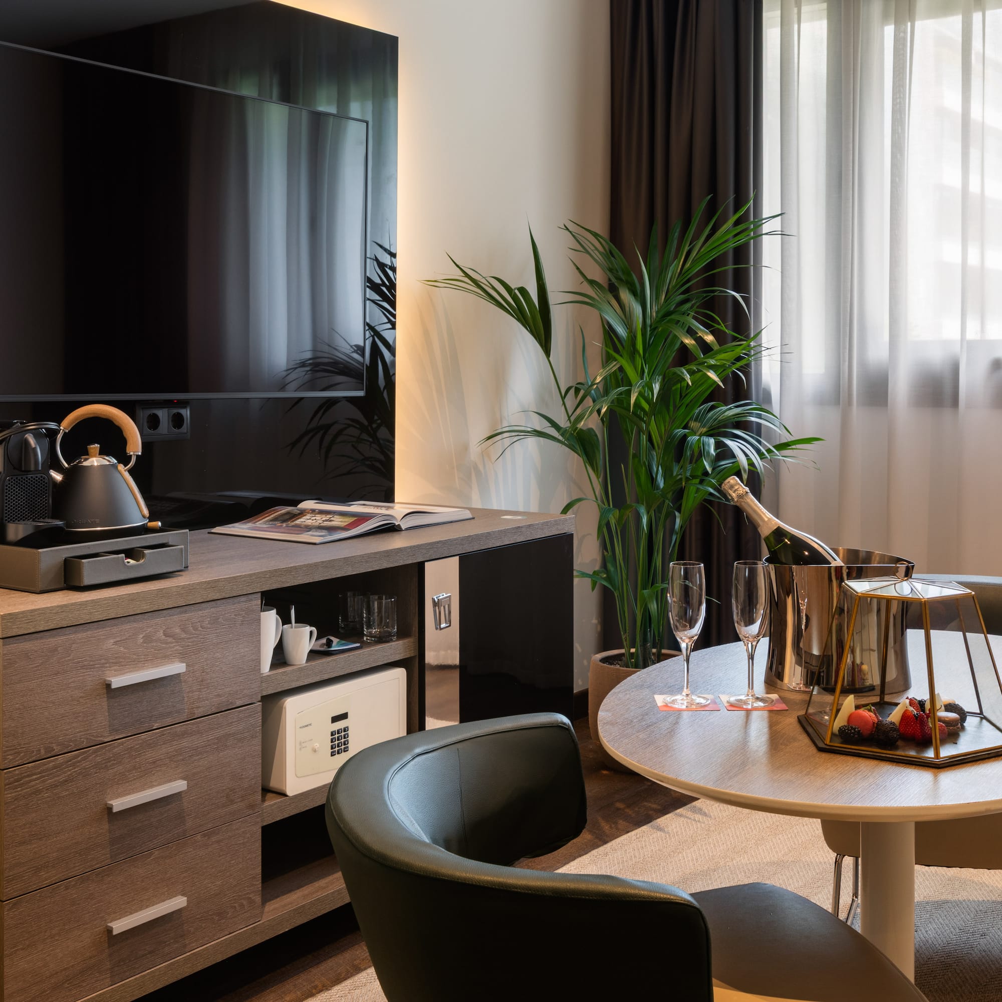 Habitación de hotel moderna con TV, cafetera, champagne, mesa y minibar.