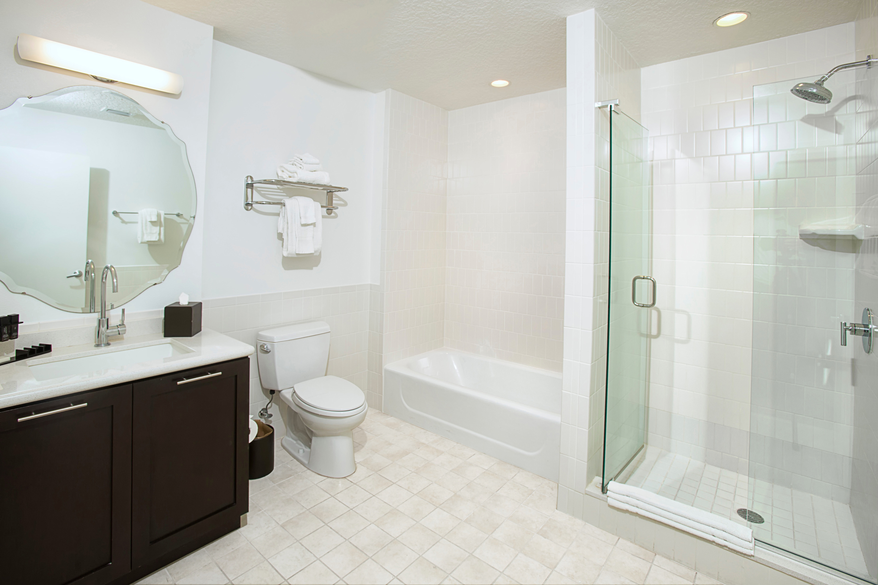 Modern white bathroom with dark vanity, mirror, toilet, tub, and glass shower.