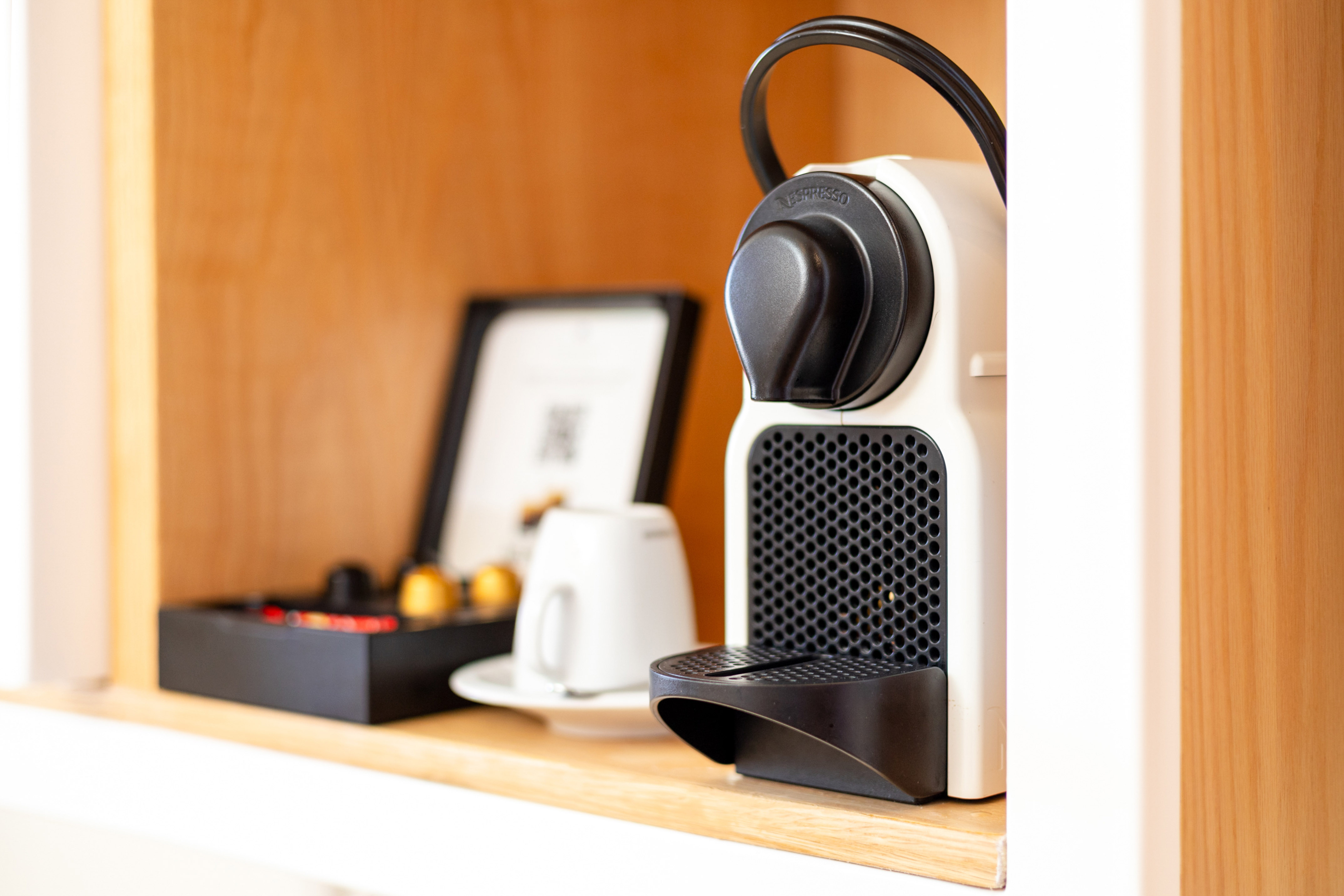Nespresso coffee machine, coffee pods, and white cup on wooden shelf.