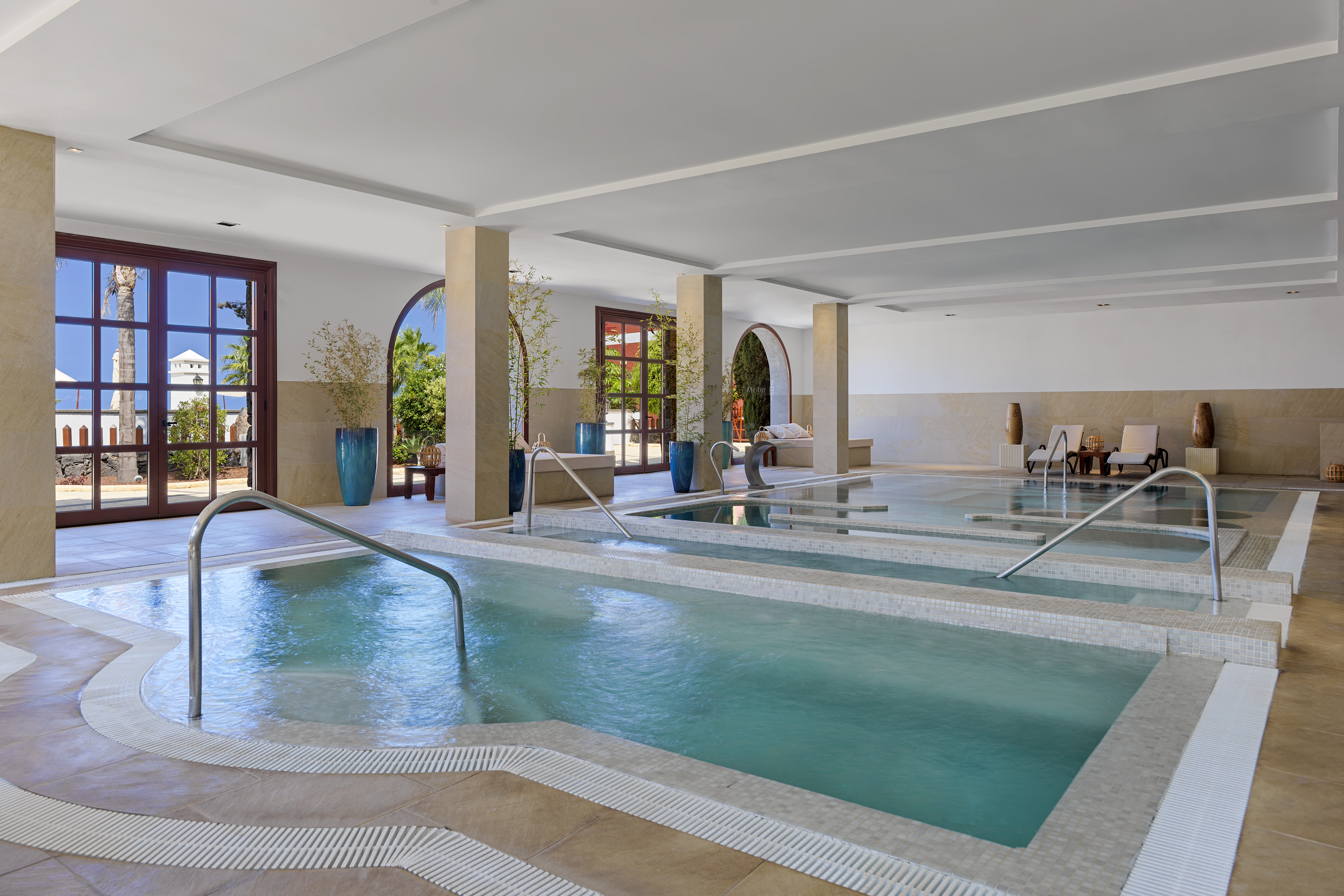 Indoor spa with tiered hydrotherapy pools, bright windows, and lounge seating.