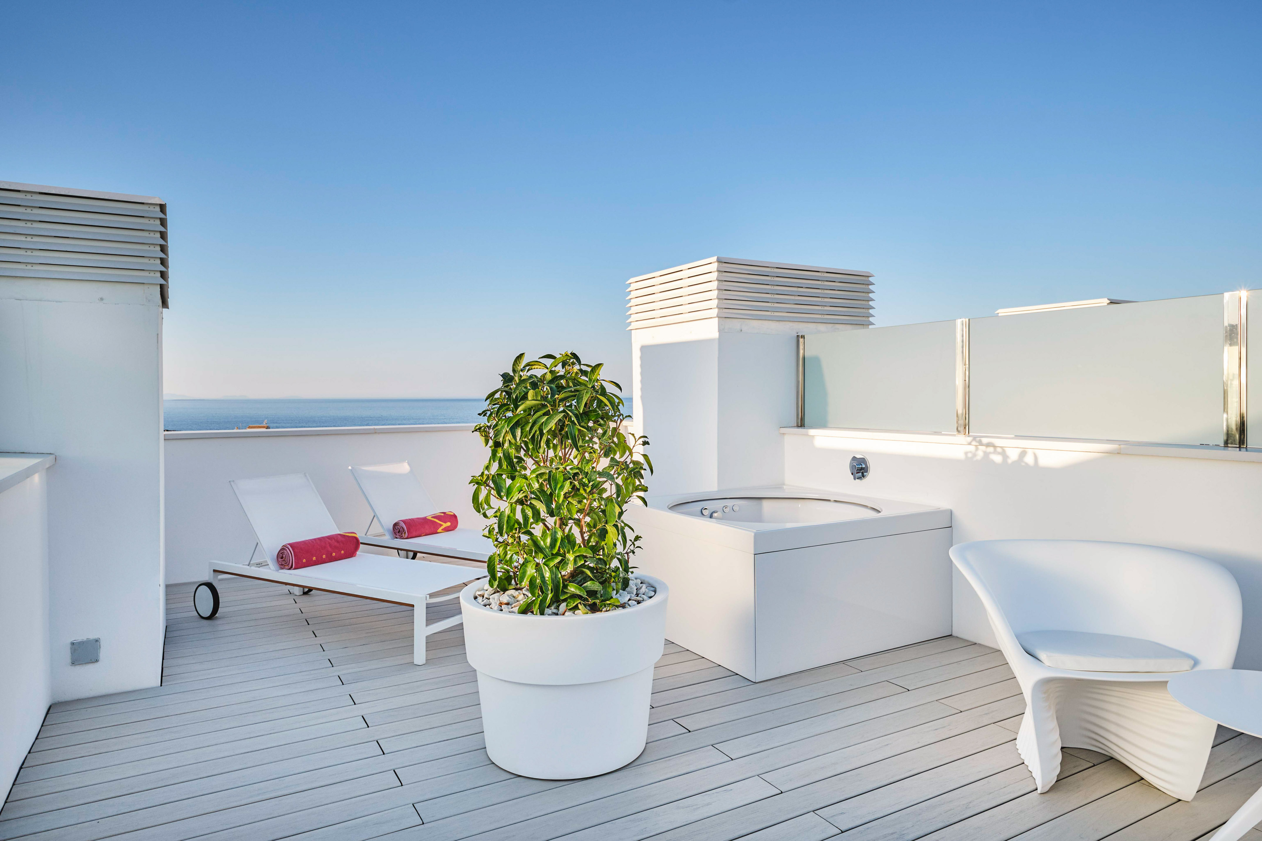 Hotel rooftop terrace with ocean view, jacuzzi, and lounge chairs.