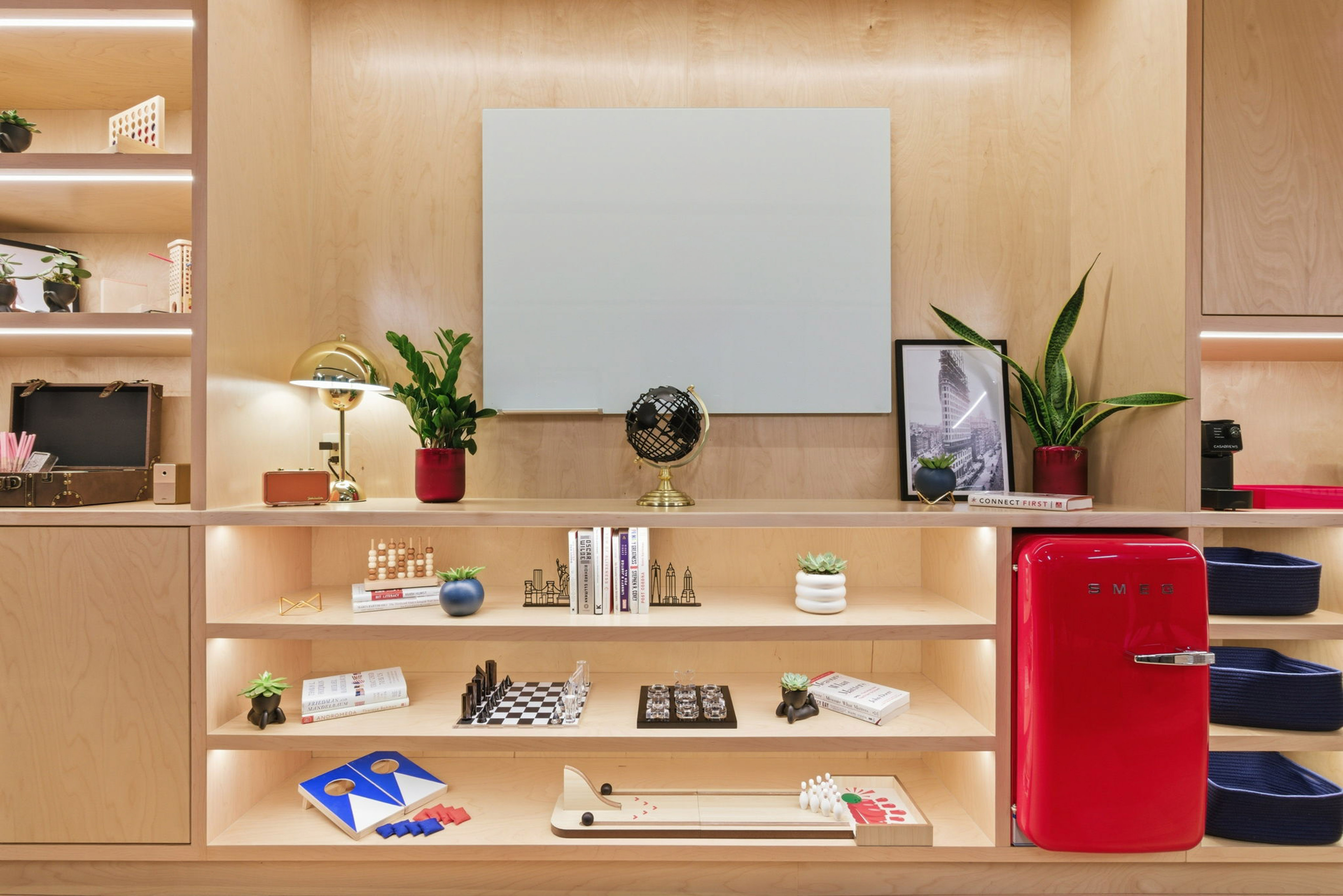 Modern wooden shelving unit with plants, games, books, and a red SMEG mini fridge.