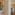 Modern hotel interior: plant, TV, and bedroom with bed and green blanket.