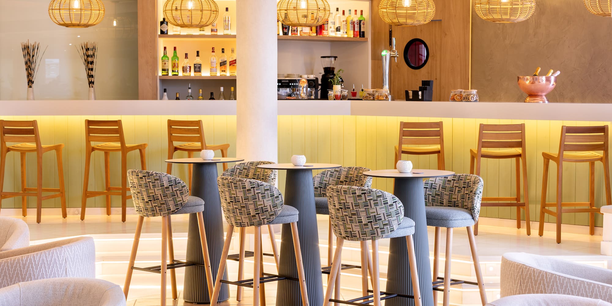 Modern hotel bar lounge with rattan lights, bar seating, and illuminated counter.
