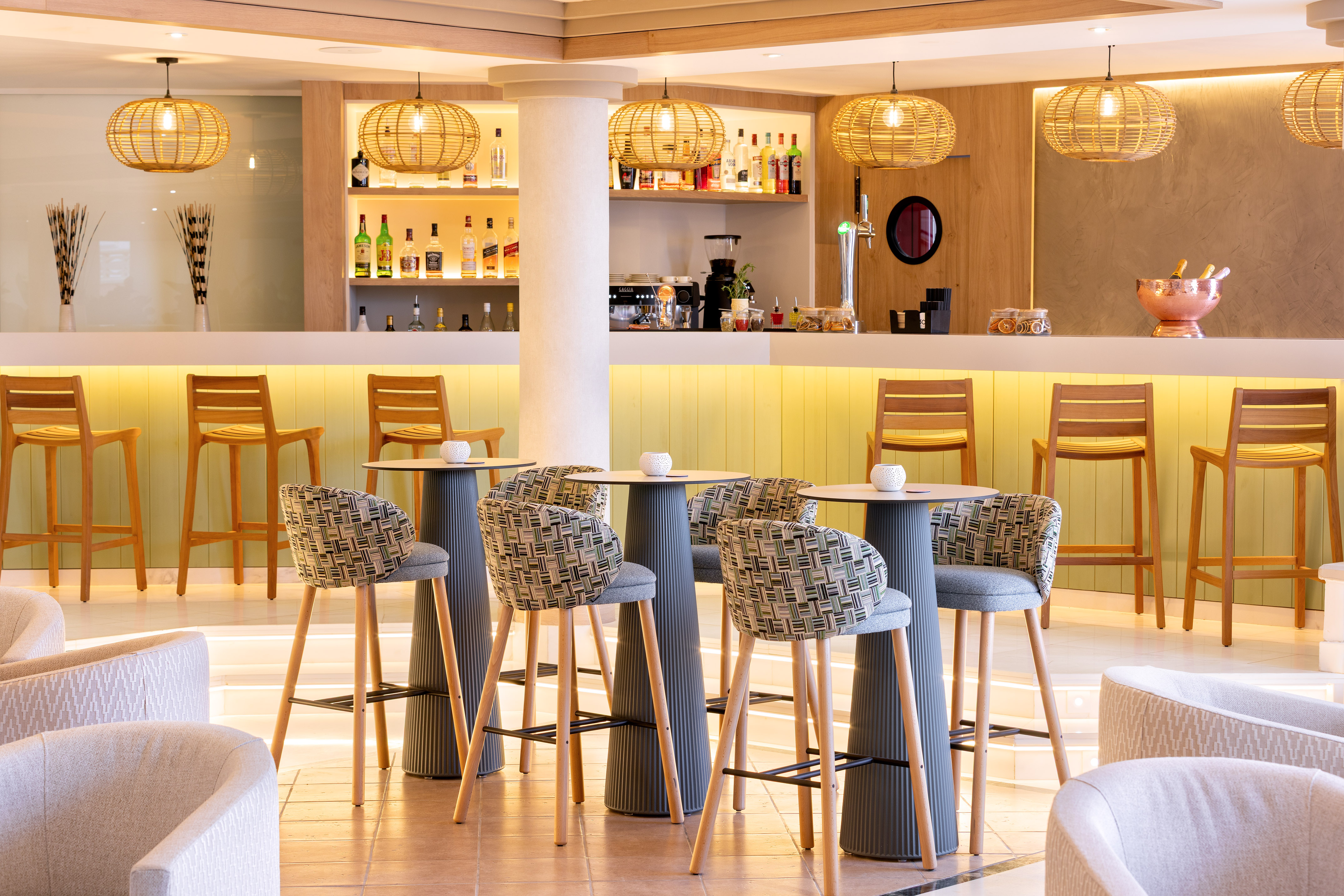Modern hotel bar lounge with rattan lights, bar seating, and illuminated counter.