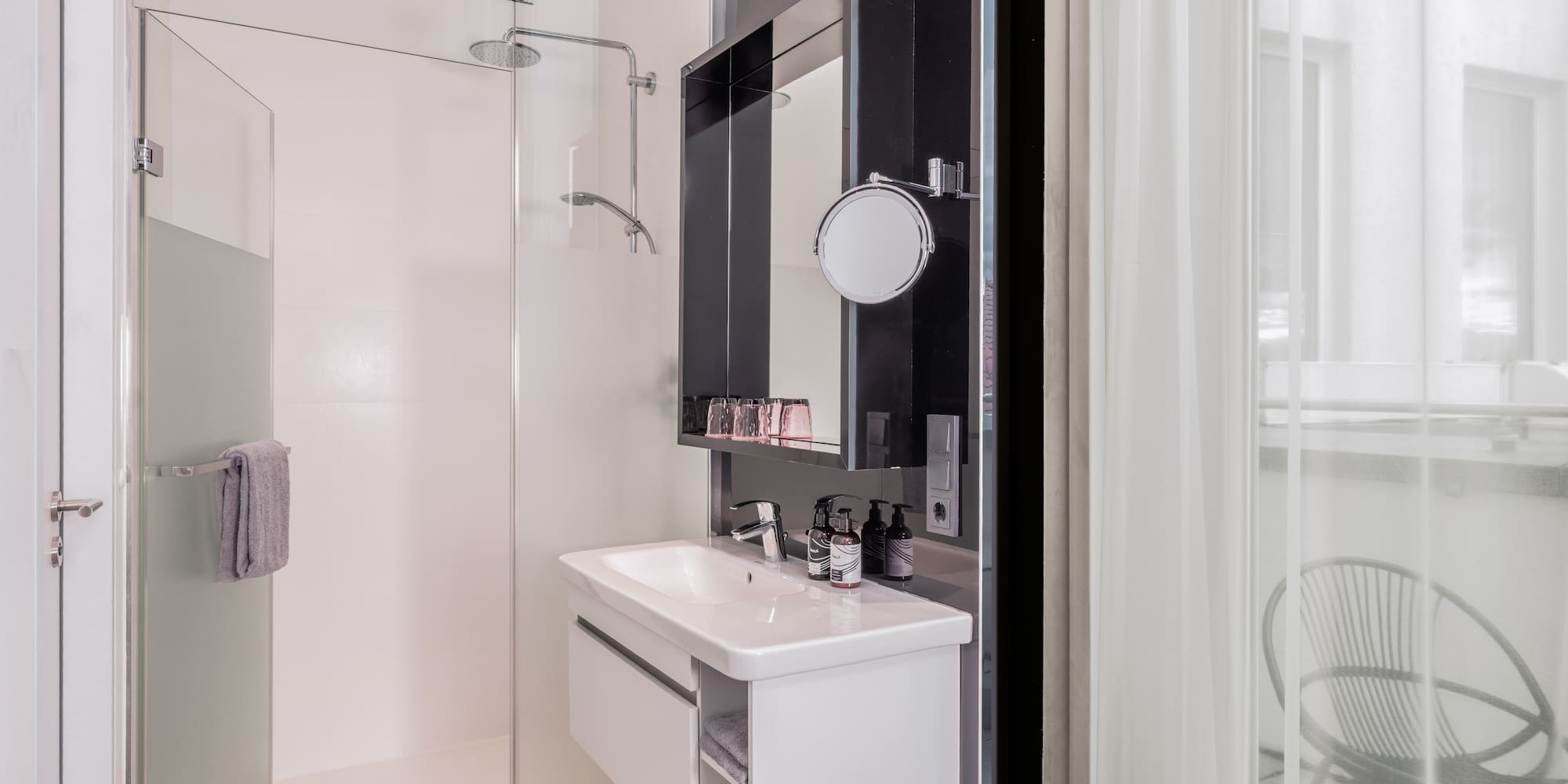 Modern hotel bathroom with glass shower, white vanity, and balcony view.