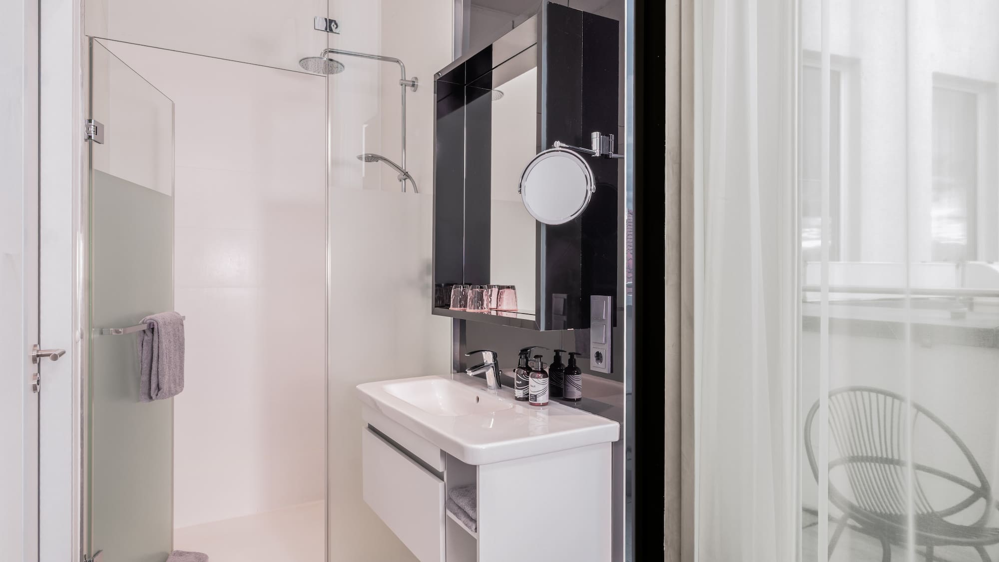 Modern hotel bathroom with glass shower, white vanity, and balcony view.