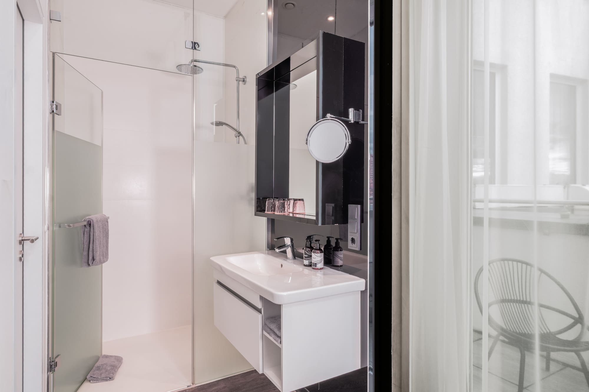 Modern hotel bathroom with glass shower, white vanity, and balcony view.