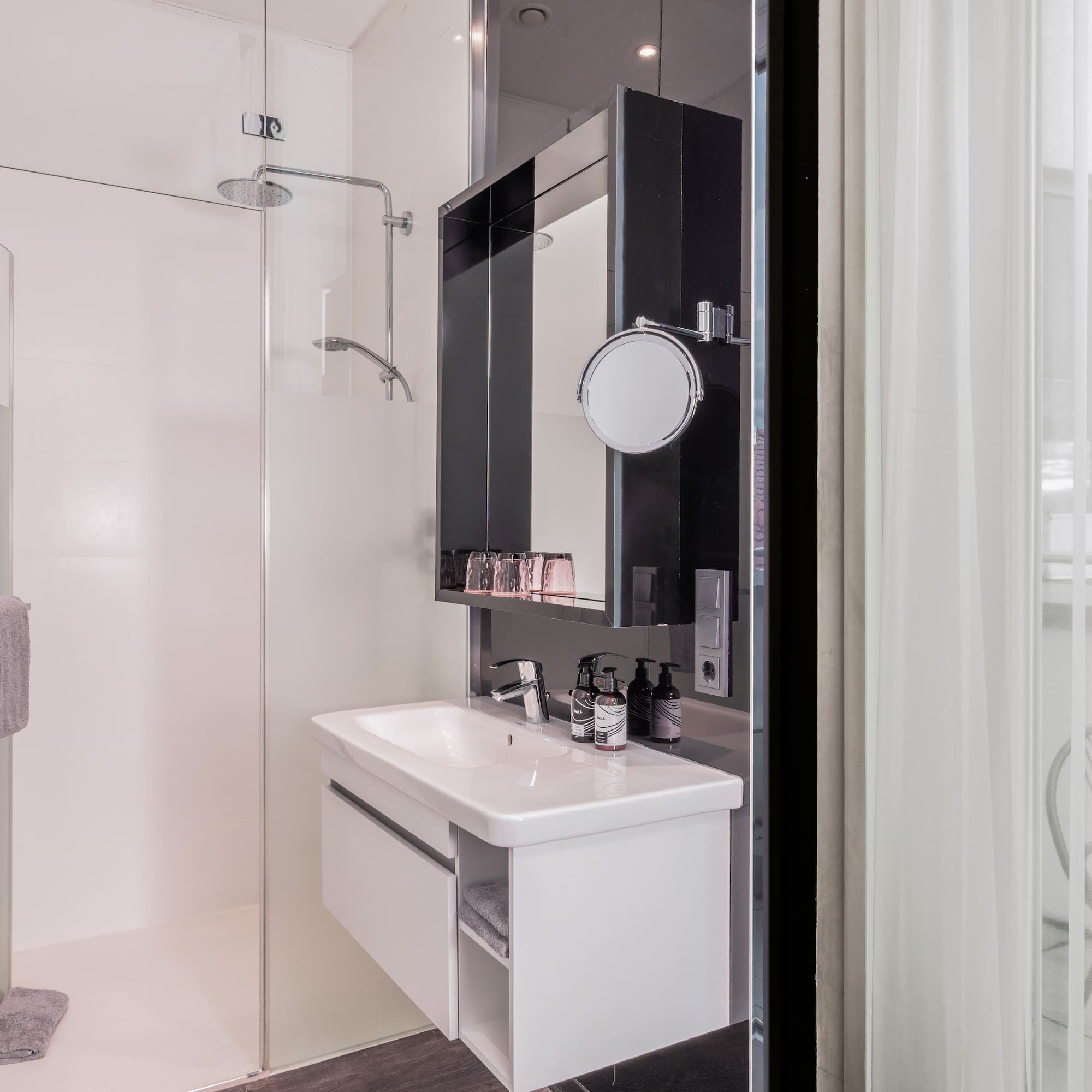 Modern hotel bathroom with glass shower, white vanity, and balcony view.