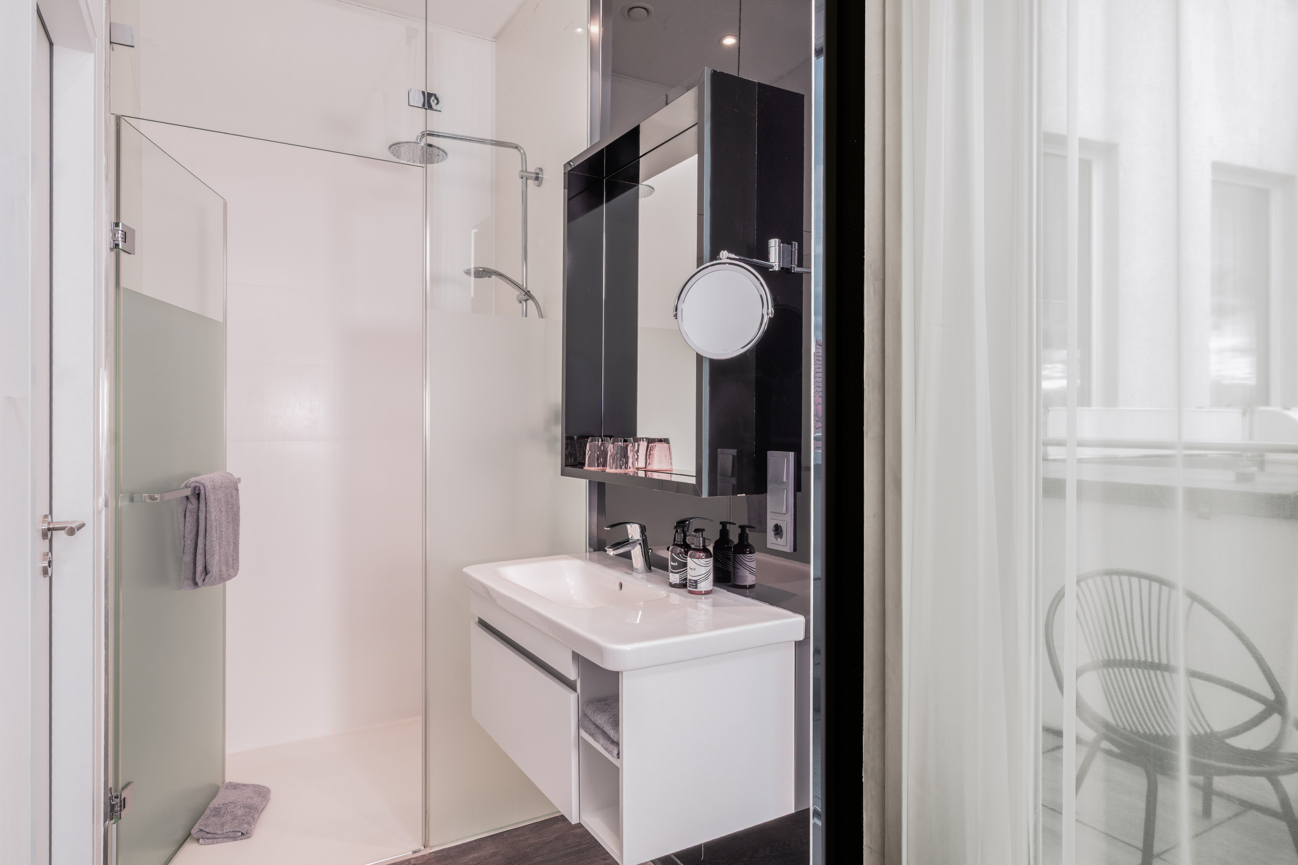 Modern hotel bathroom with glass shower, white vanity, and balcony view.
