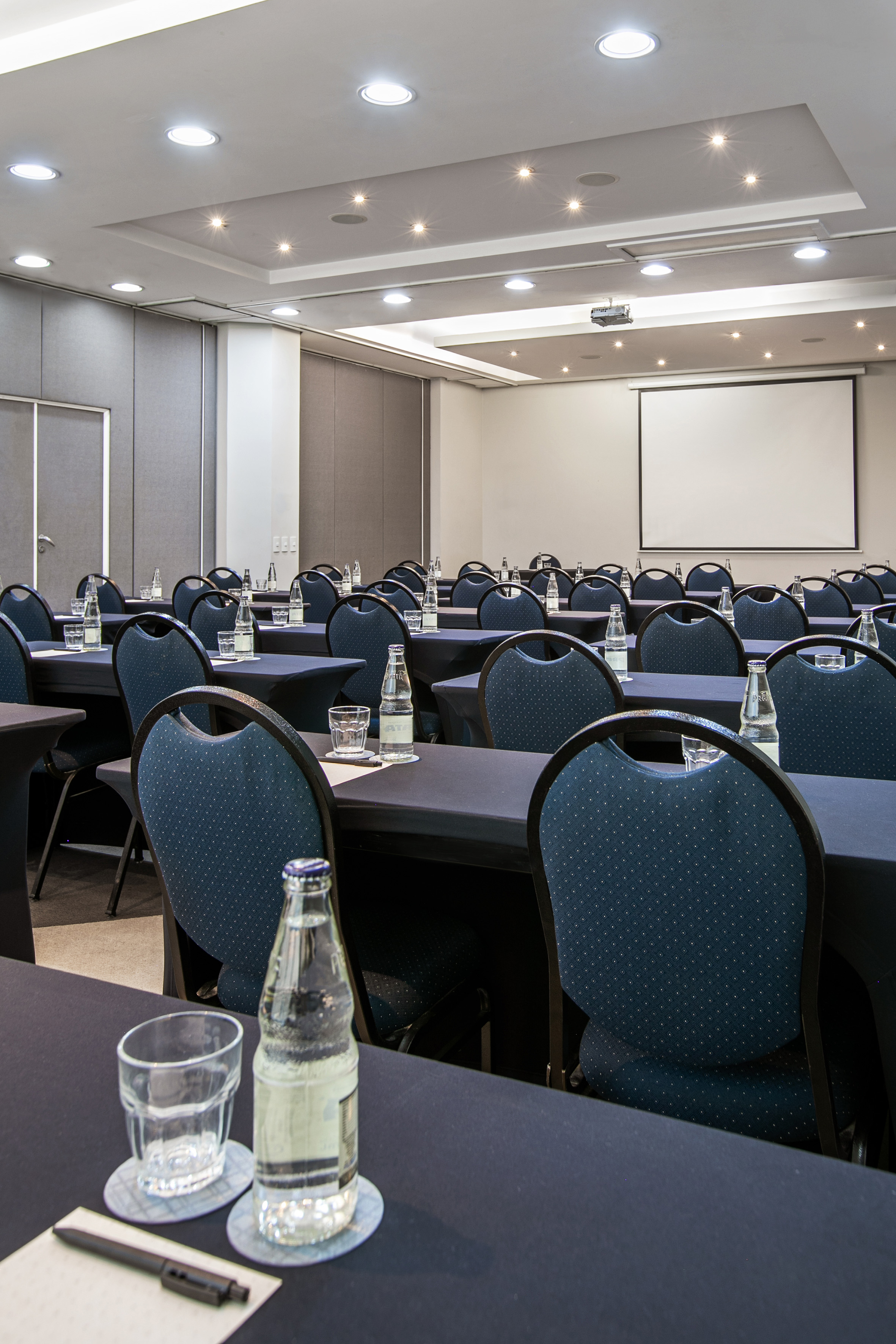 Conference room prepared for a meeting, blue chairs, tables, and projector screen.