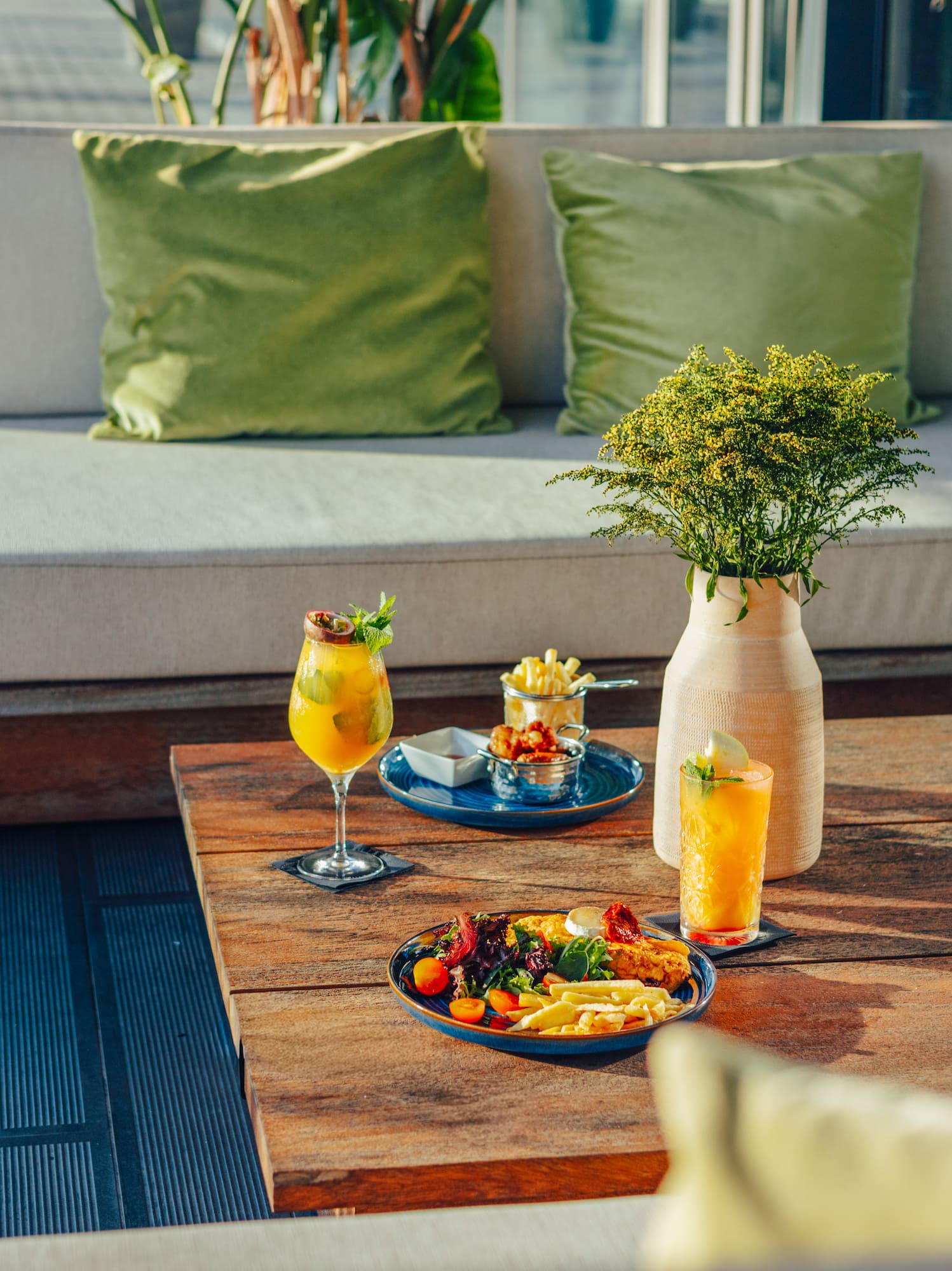 Rooftop lounge with appetizers, cocktails, wooden table, and sofa.