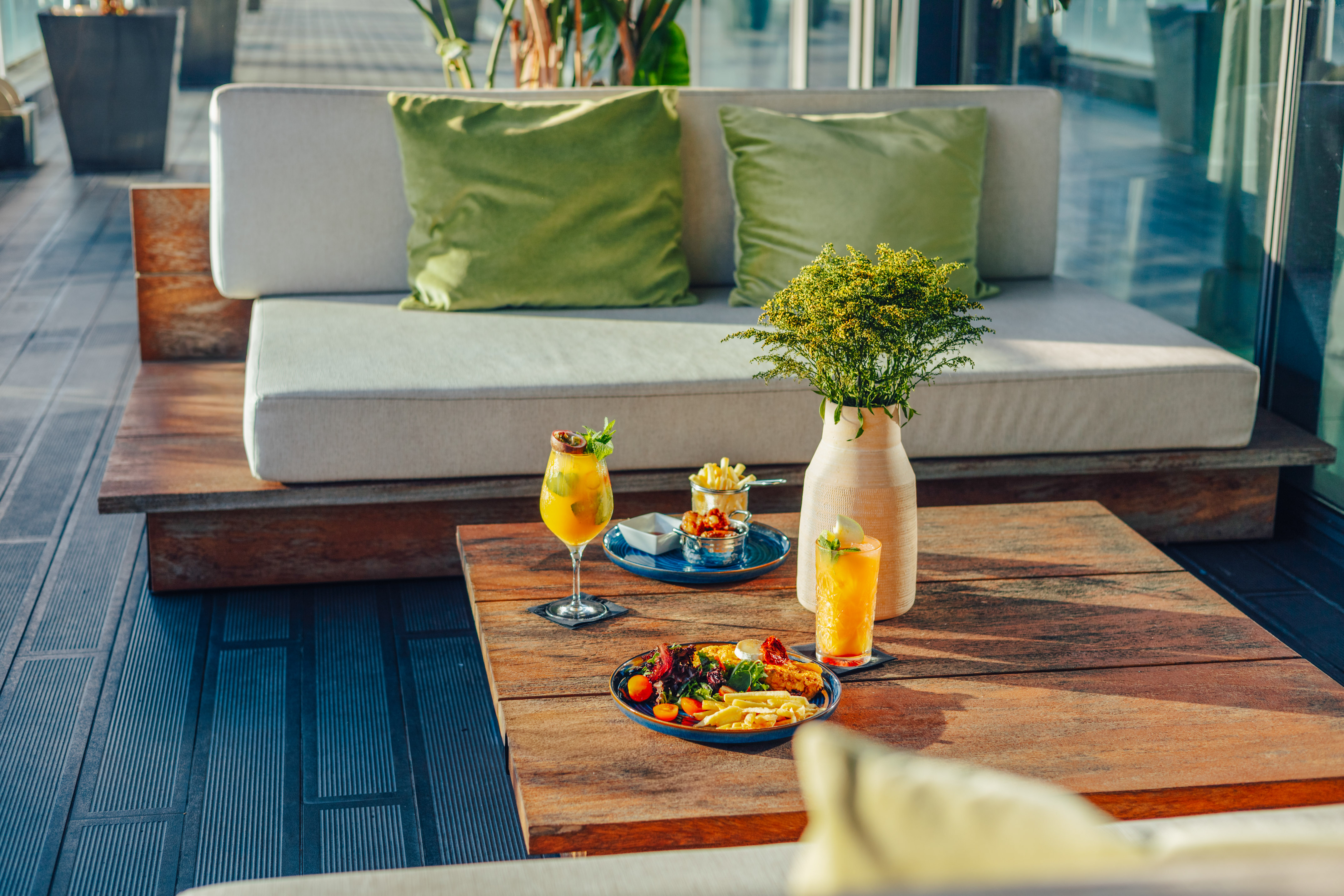 Rooftop lounge with appetizers, cocktails, wooden table, and sofa.