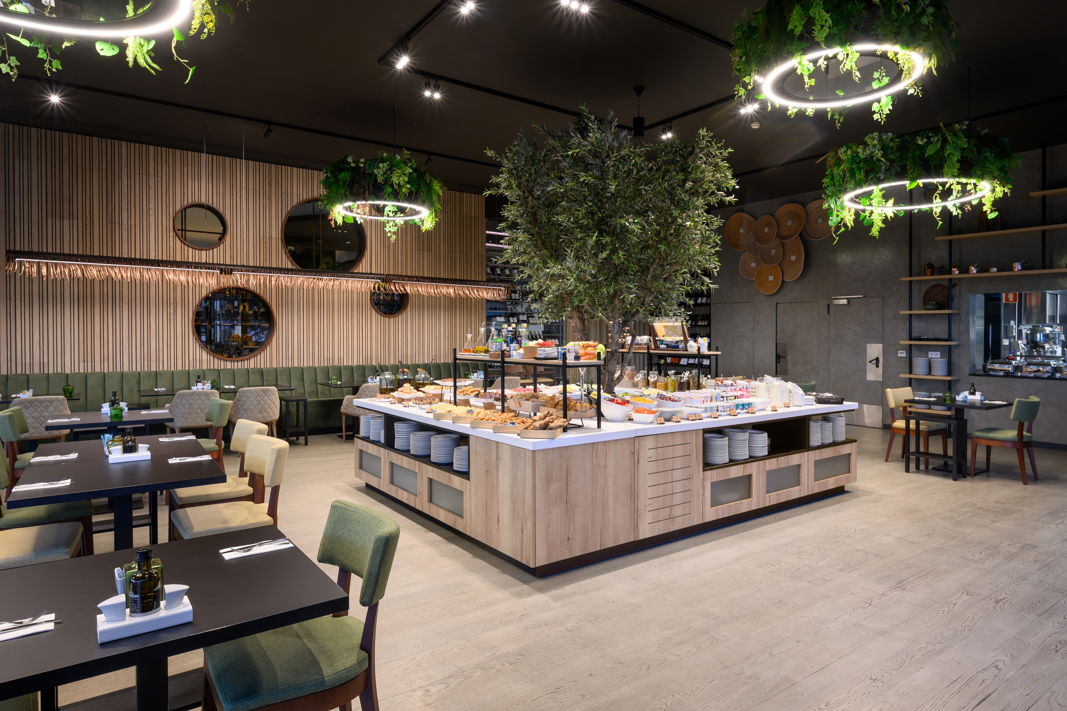 Modern restaurant buffet with olive tree, fresh food, and stylish decor.