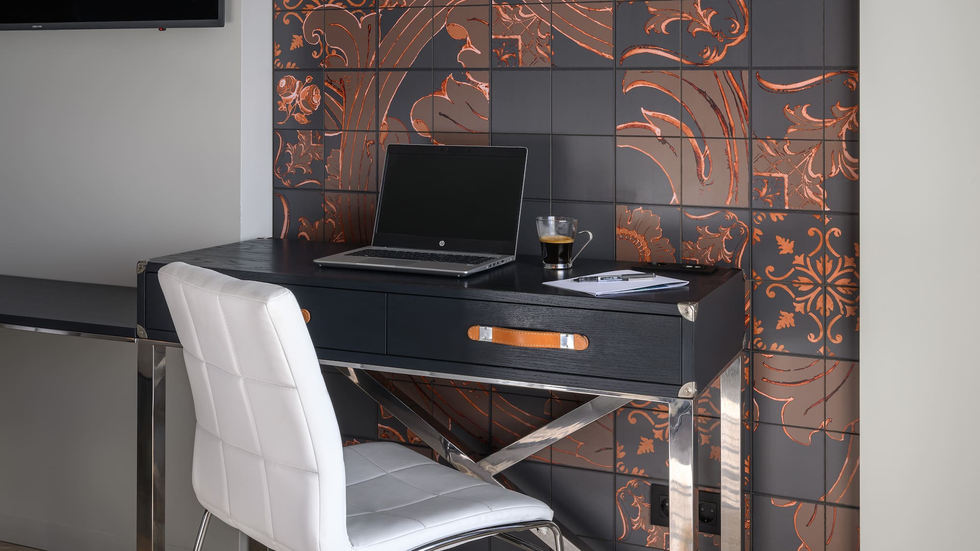 Modern black desk with laptop, white chair, and dark decorative copper wall tiles.