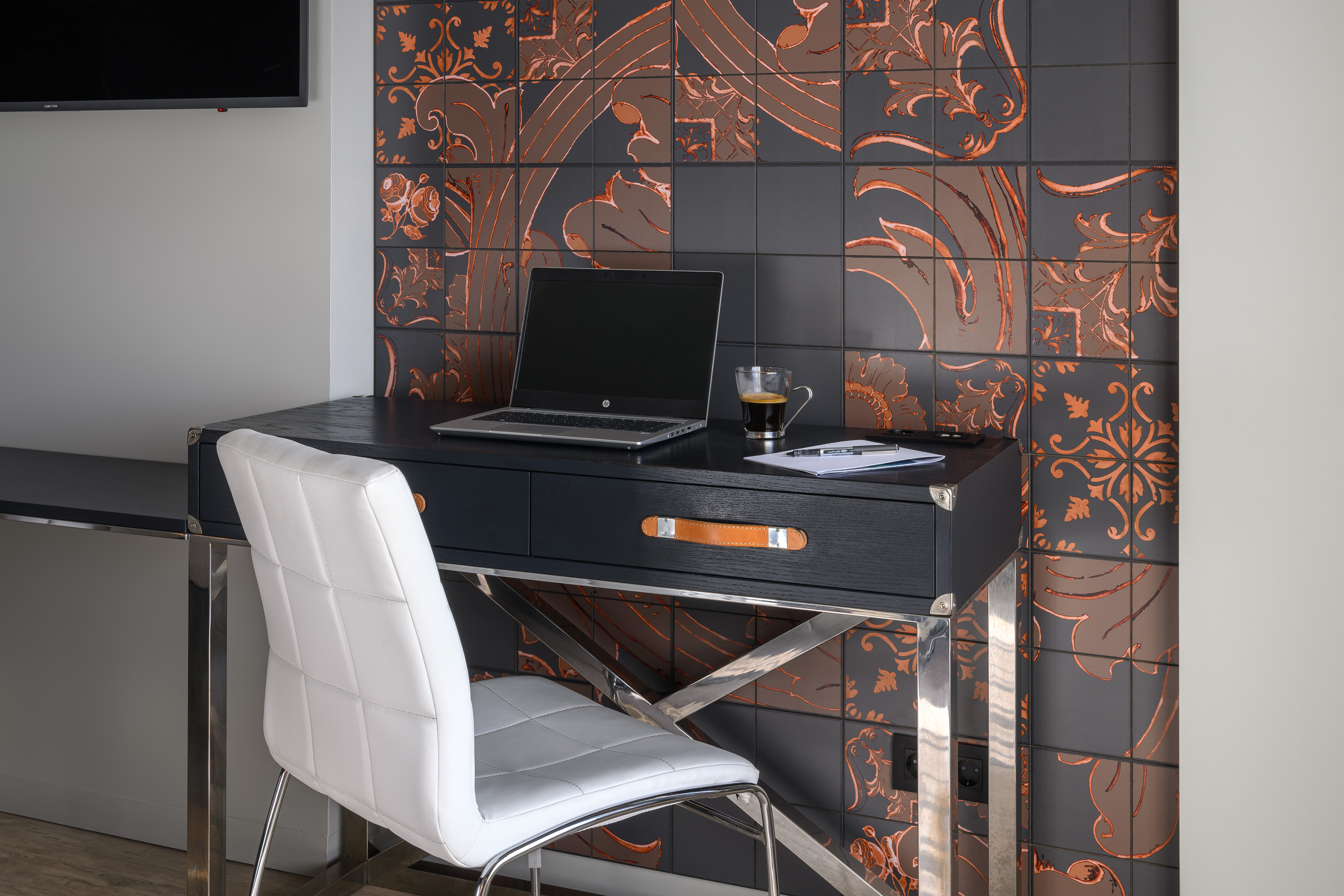 Modern black desk with laptop, white chair, and dark decorative copper wall tiles.