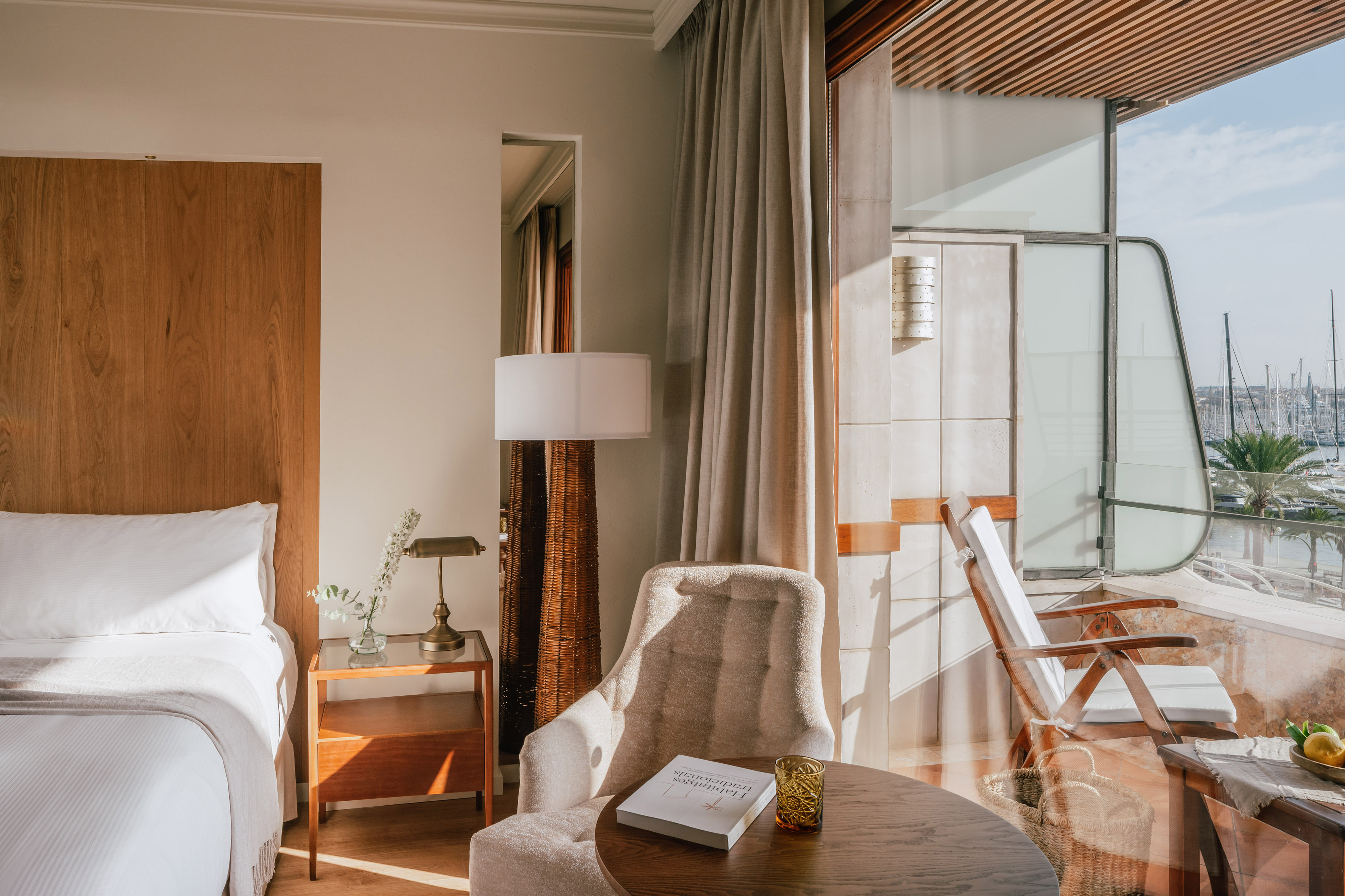Bright hotel room with balcony overlooking marina and boats.