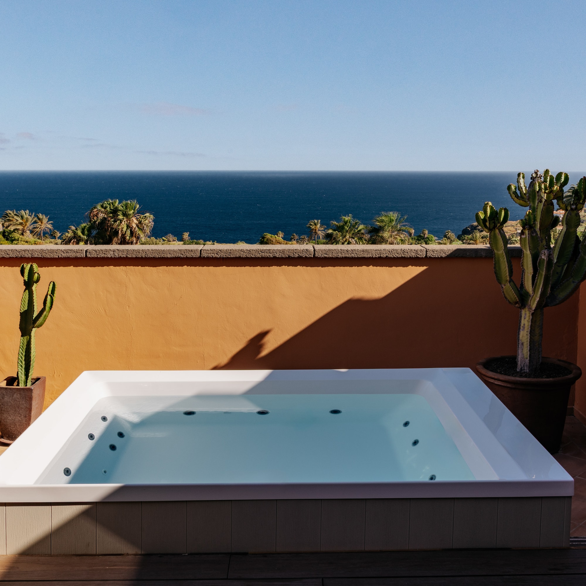 Ocean view hot tub on terracotta terrace with palm trees and cacti.