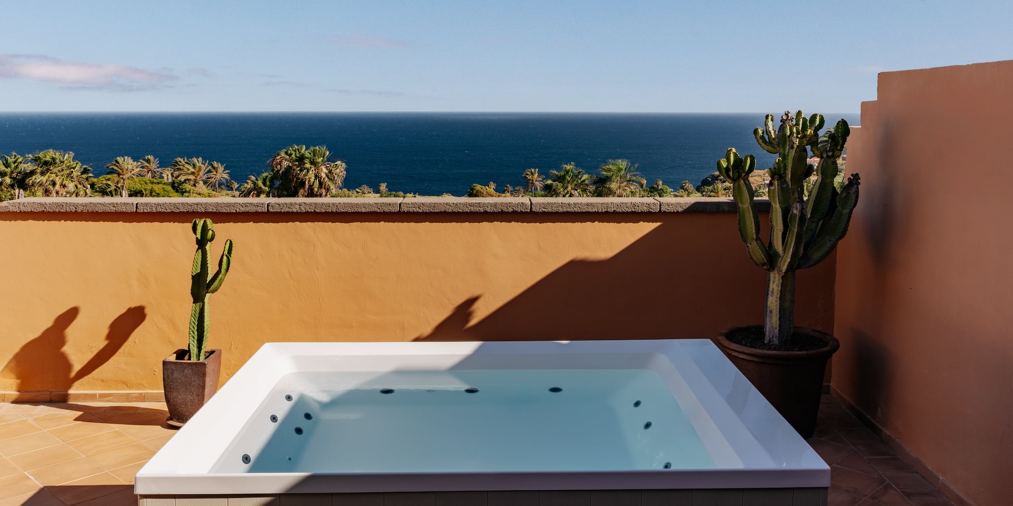 Ocean view hot tub on terracotta terrace with palm trees and cacti.