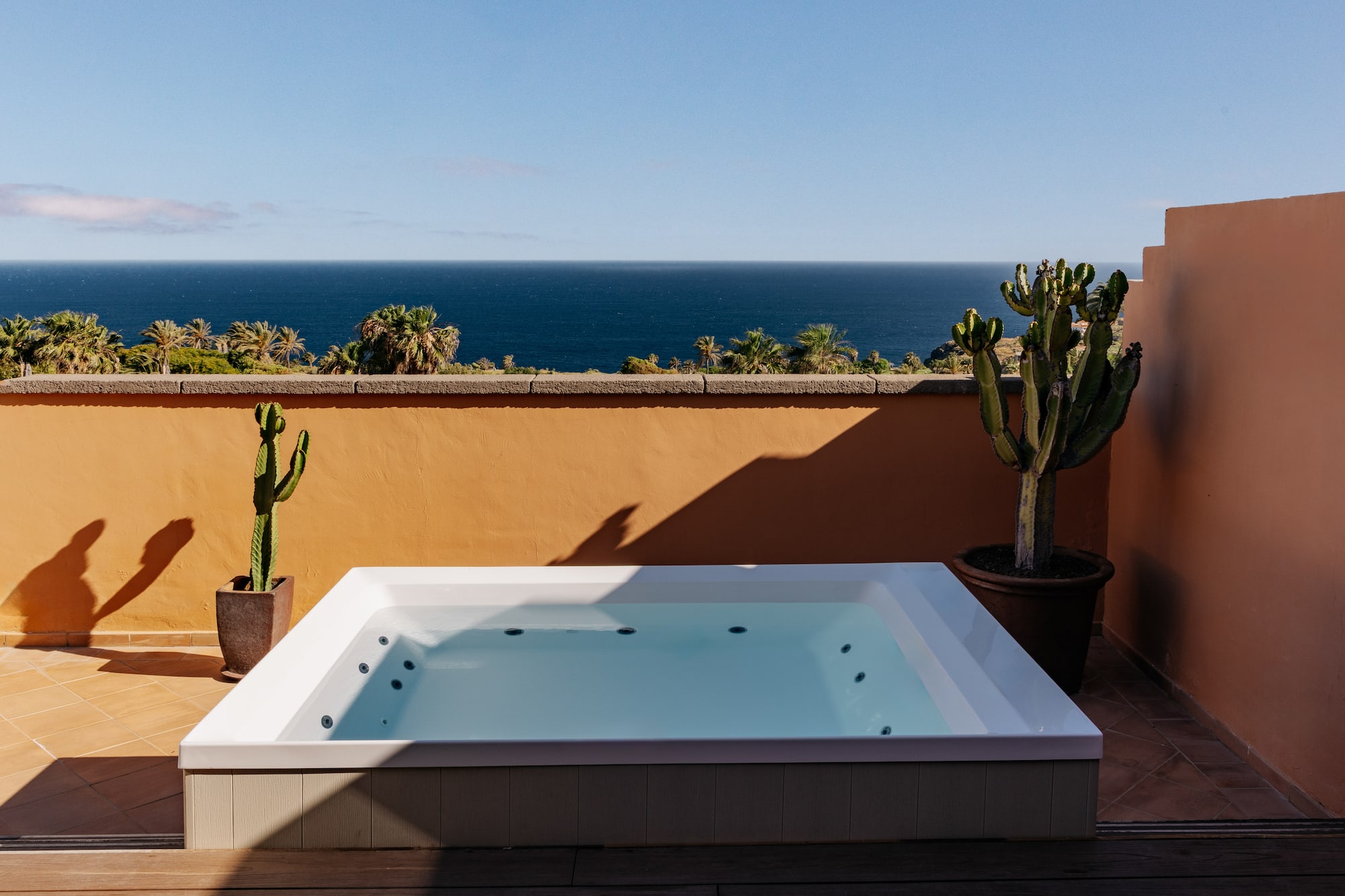 Ocean view hot tub on terracotta terrace with palm trees and cacti.