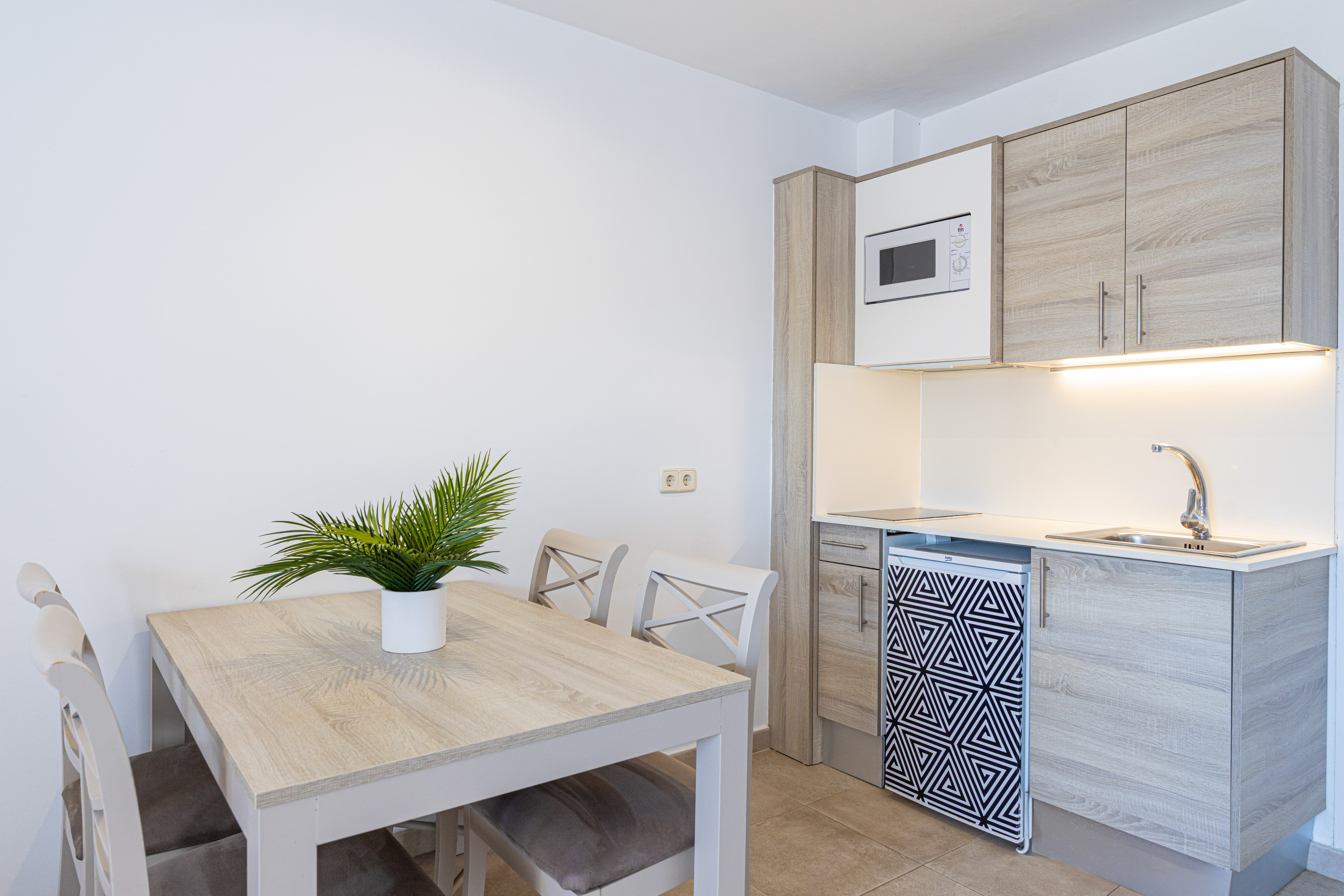 Modern kitchenette and dining area with light wood table and geometric fridge.