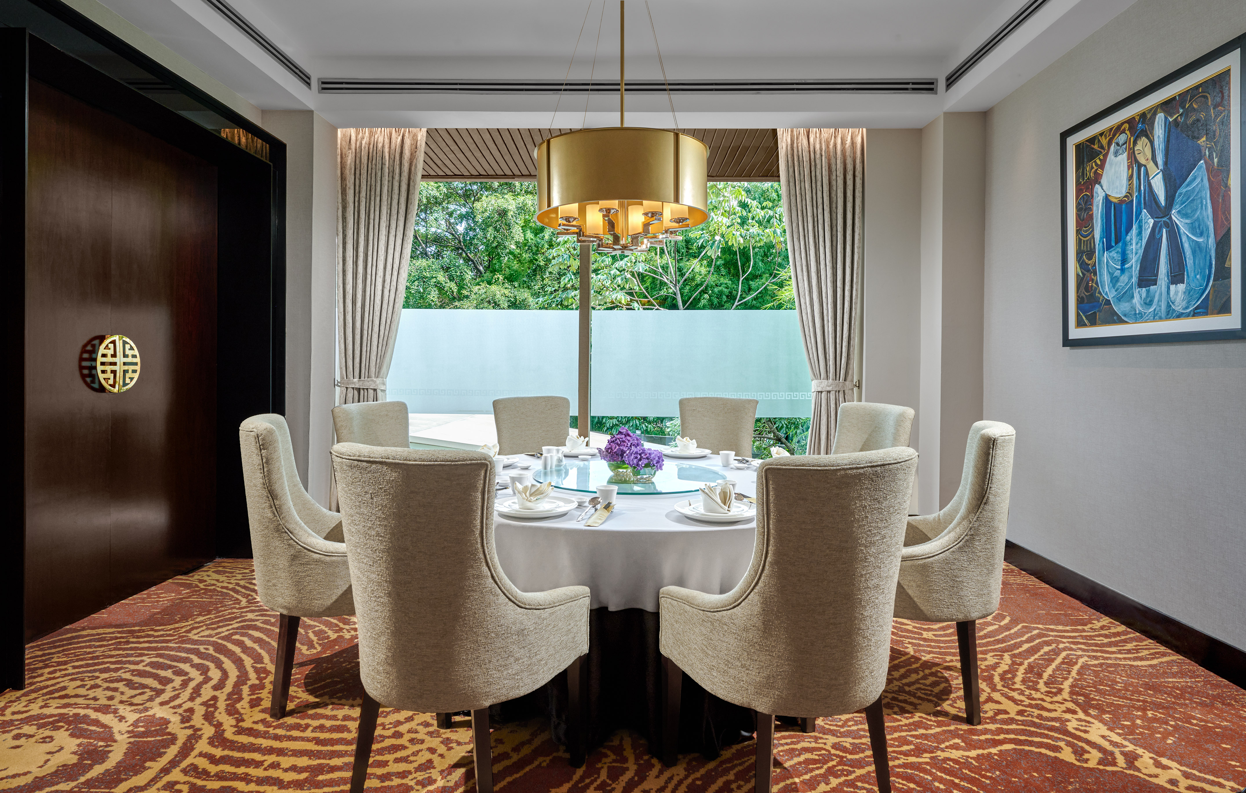 Private dining room with round table, gold chandelier, and large window.