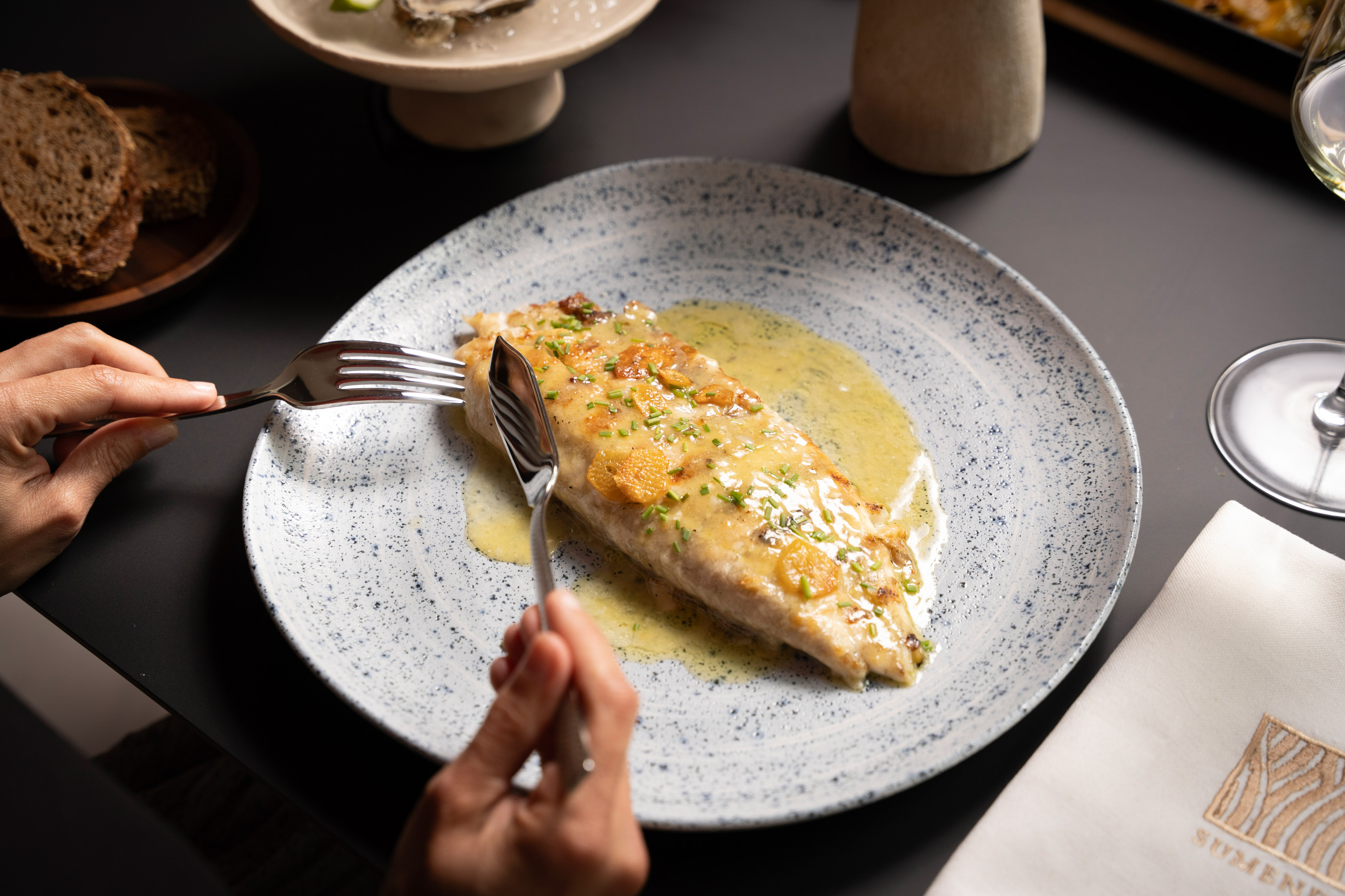 Gourmet fish fillet with lemon-butter sauce, chives, garlic on speckled plate.