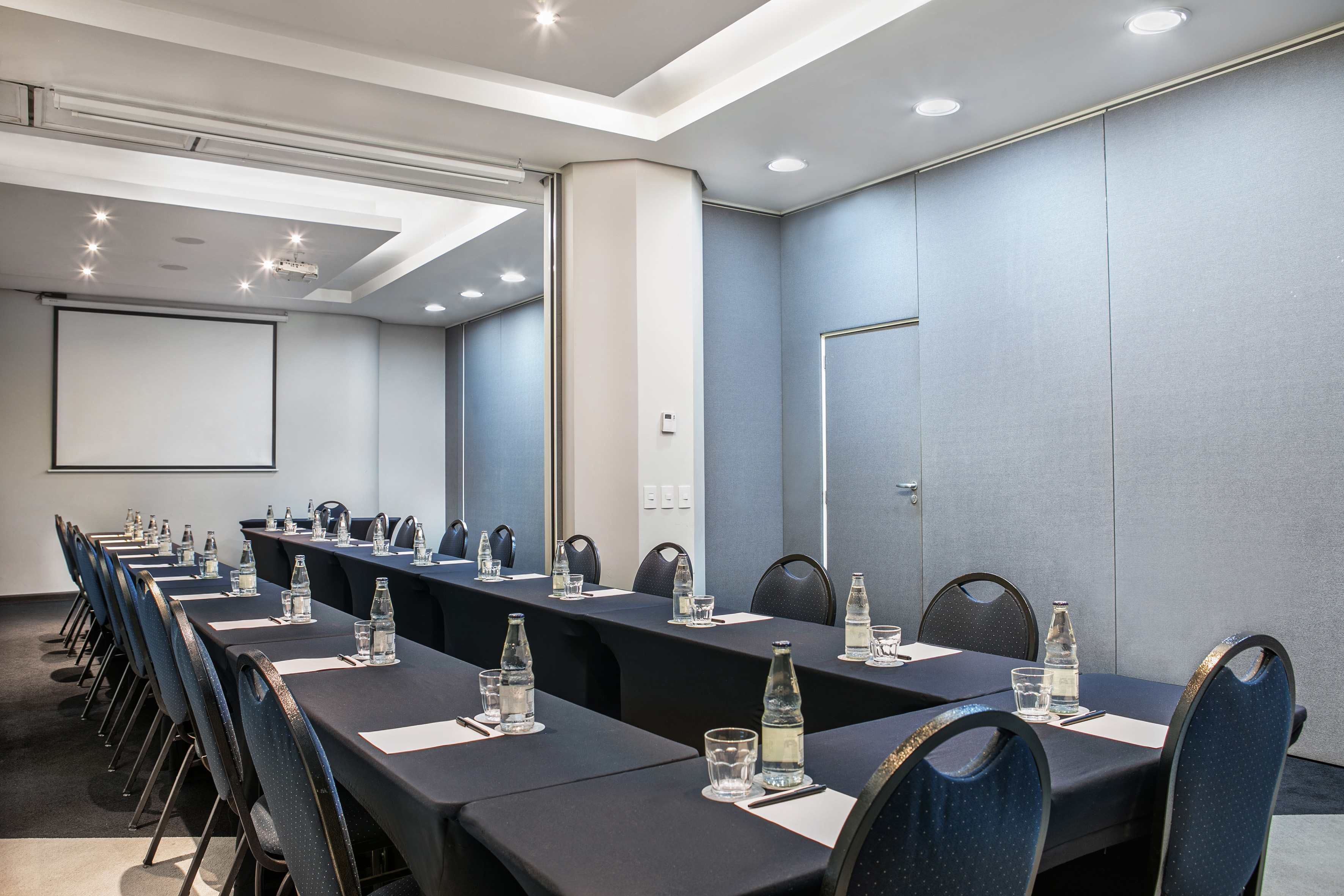 Modern business conference room with U-shaped table, projector screen.