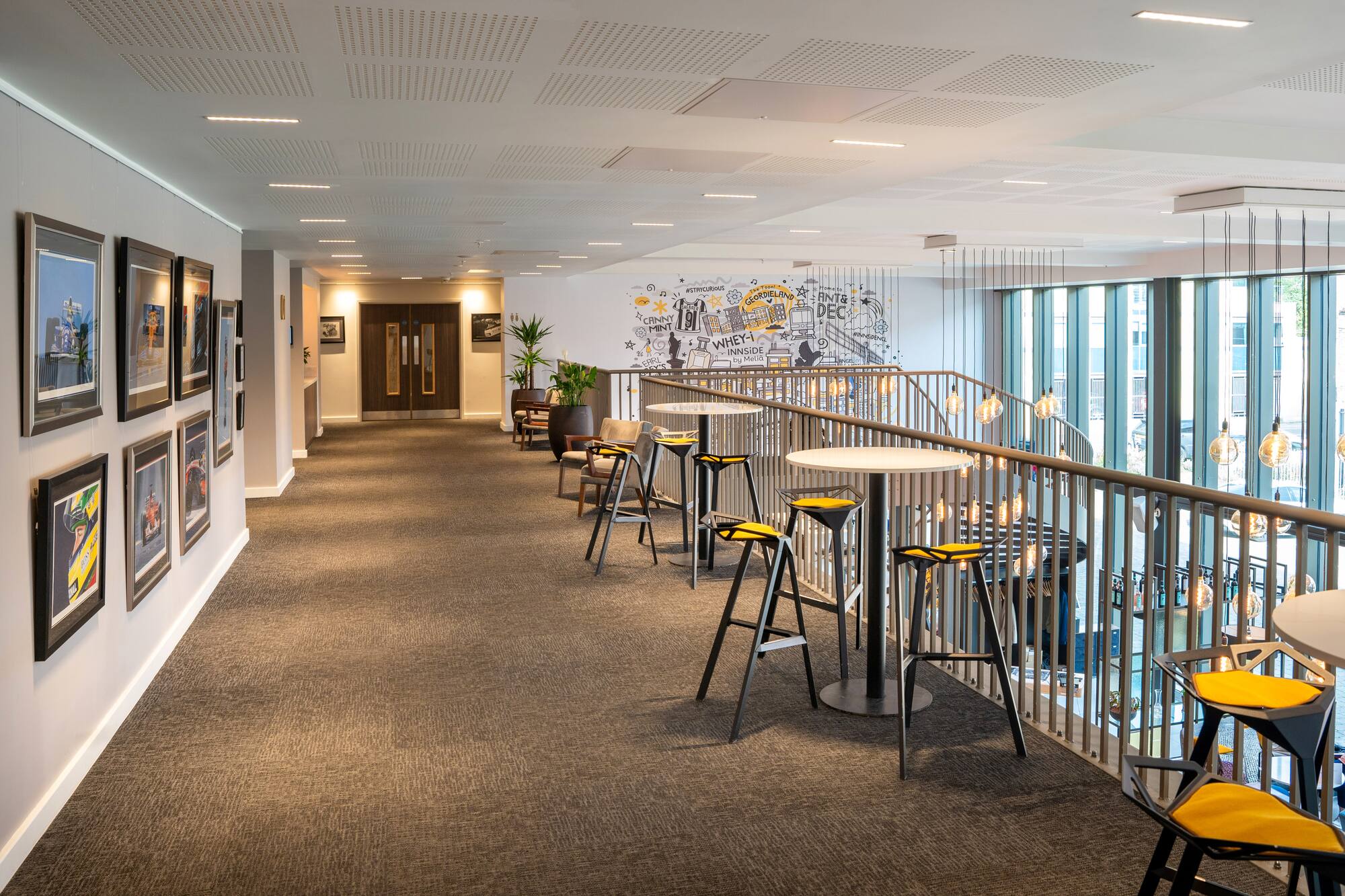 Modern hotel lounge with vibrant mural, high tables, and framed hallway art.