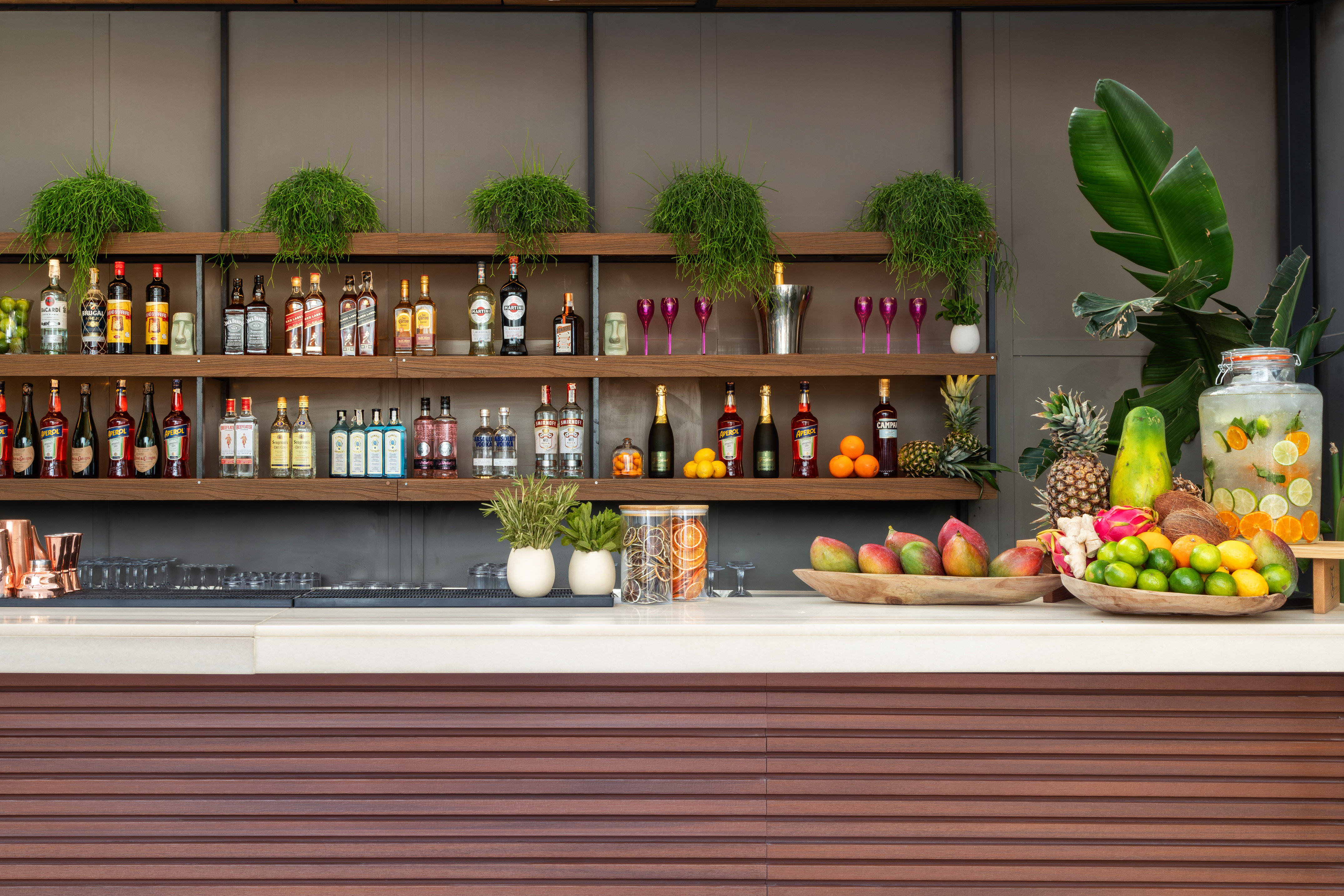 Tropical bar with liquor bottles, fresh fruit, and a vibrant cocktail dispenser.