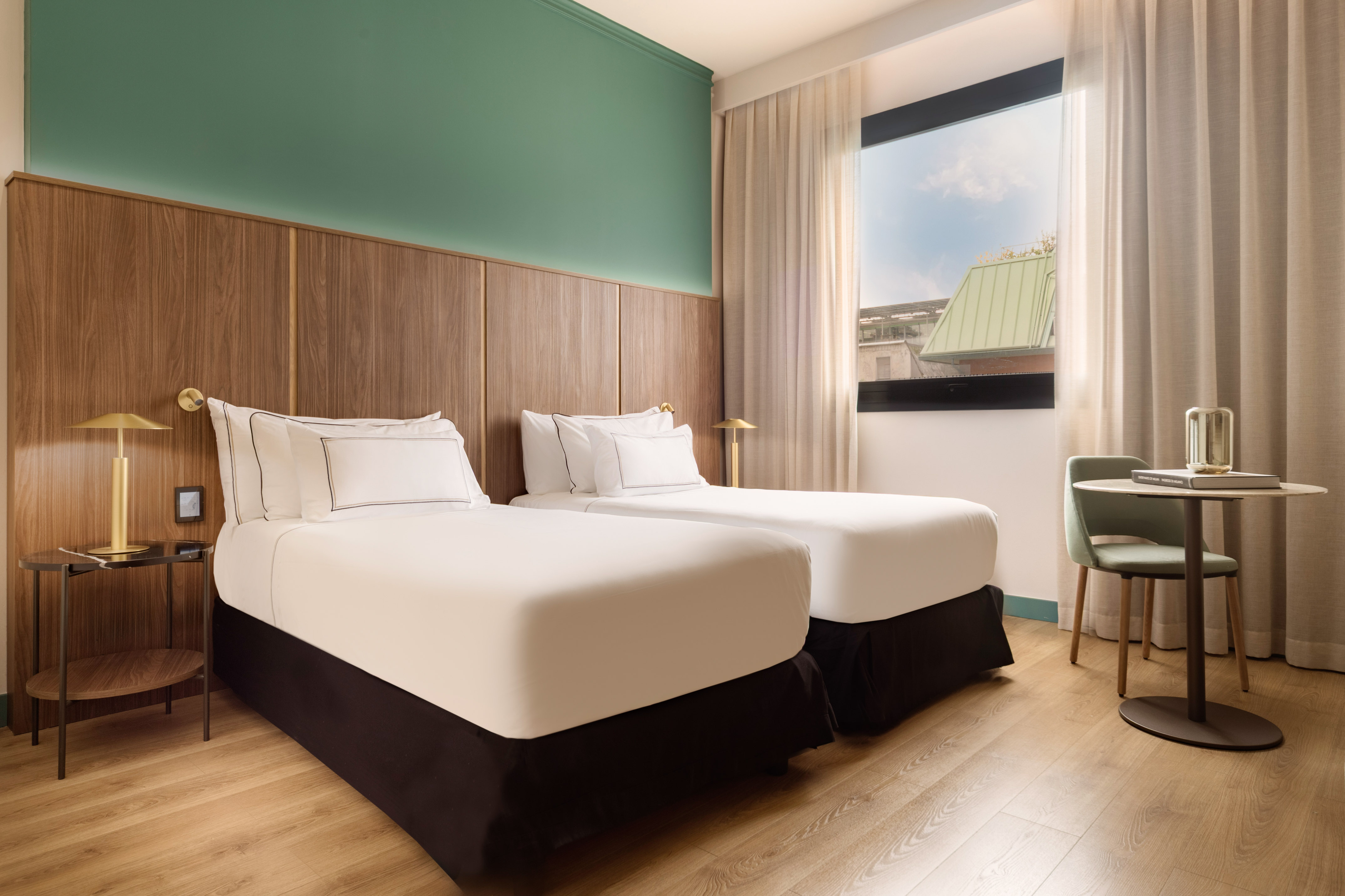 Hotel guest room with two twin beds, wood headboard, green wall, and window.