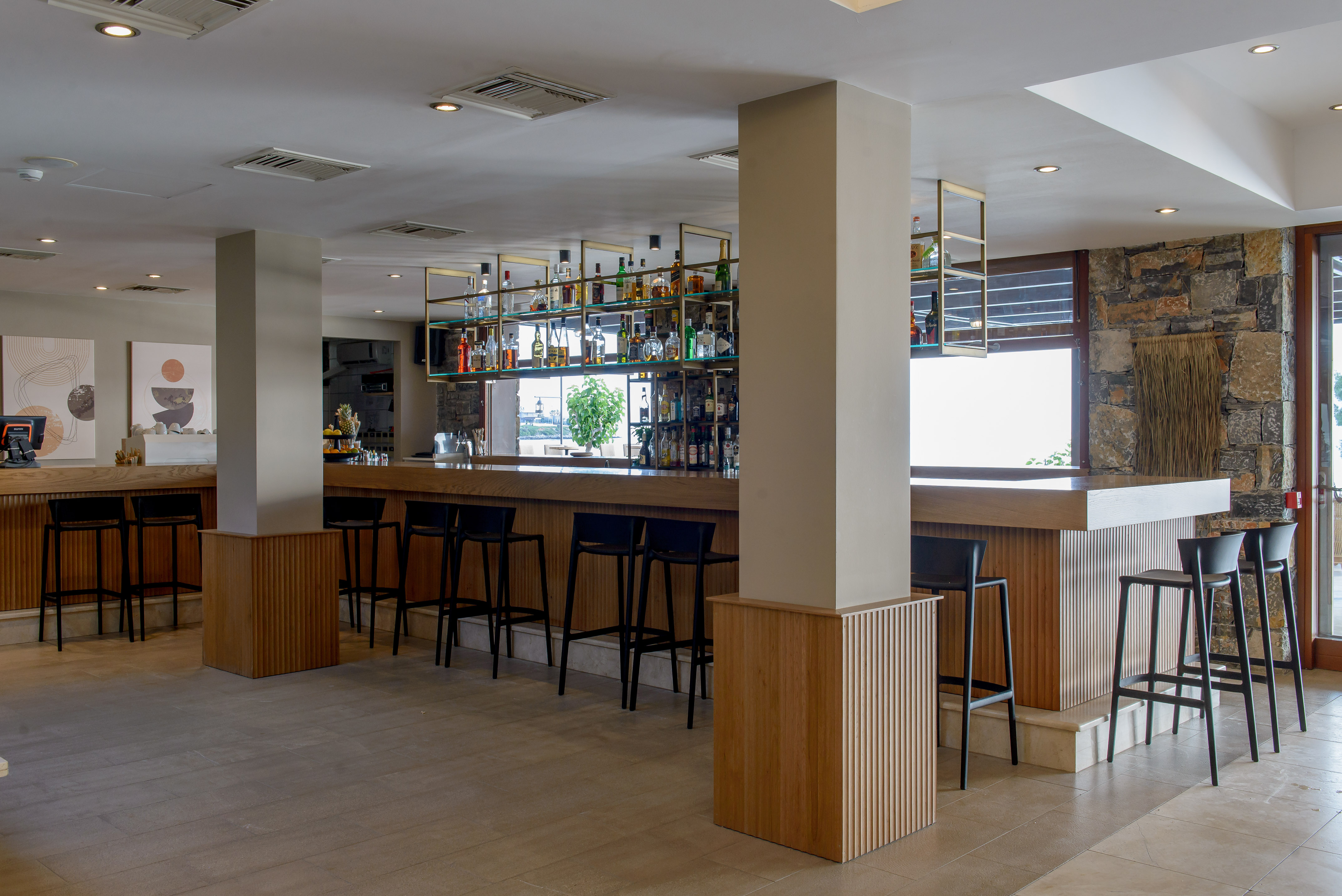 Modern hotel bar with wooden counter, black stools, and liquor display.