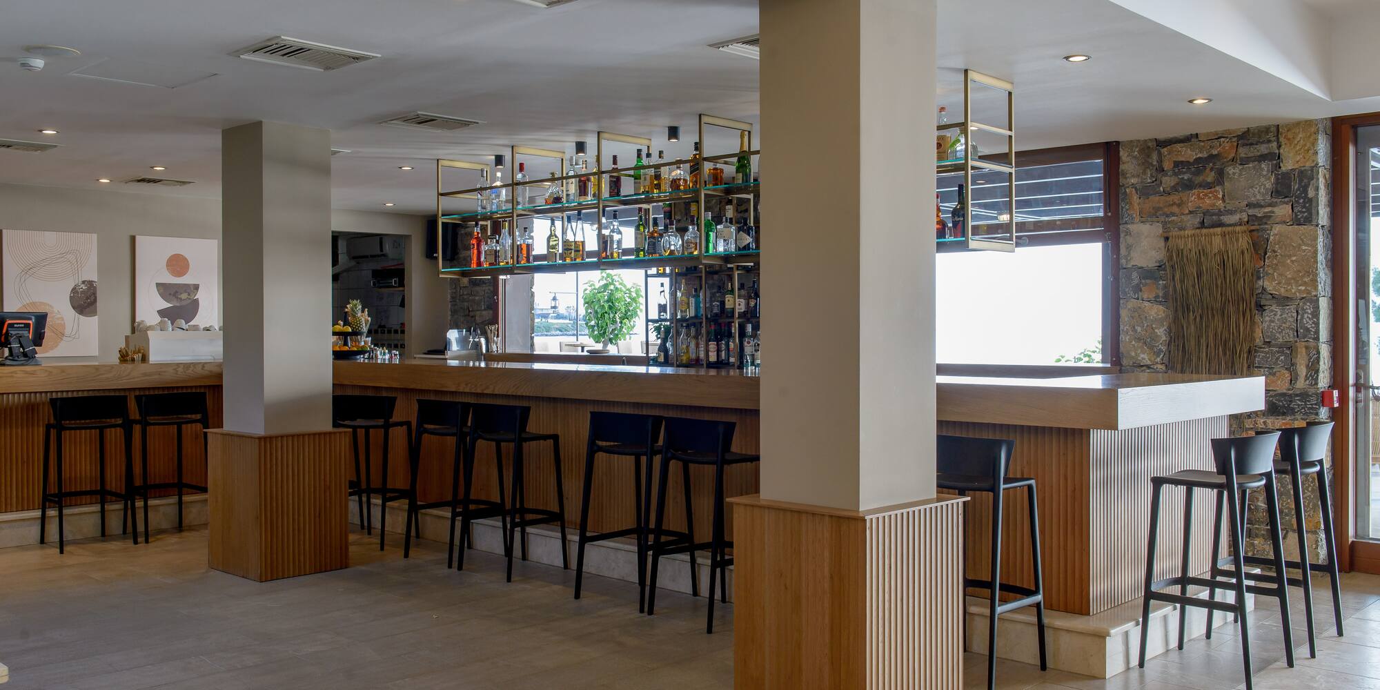 Modern hotel bar with wooden counter, black stools, and liquor display.