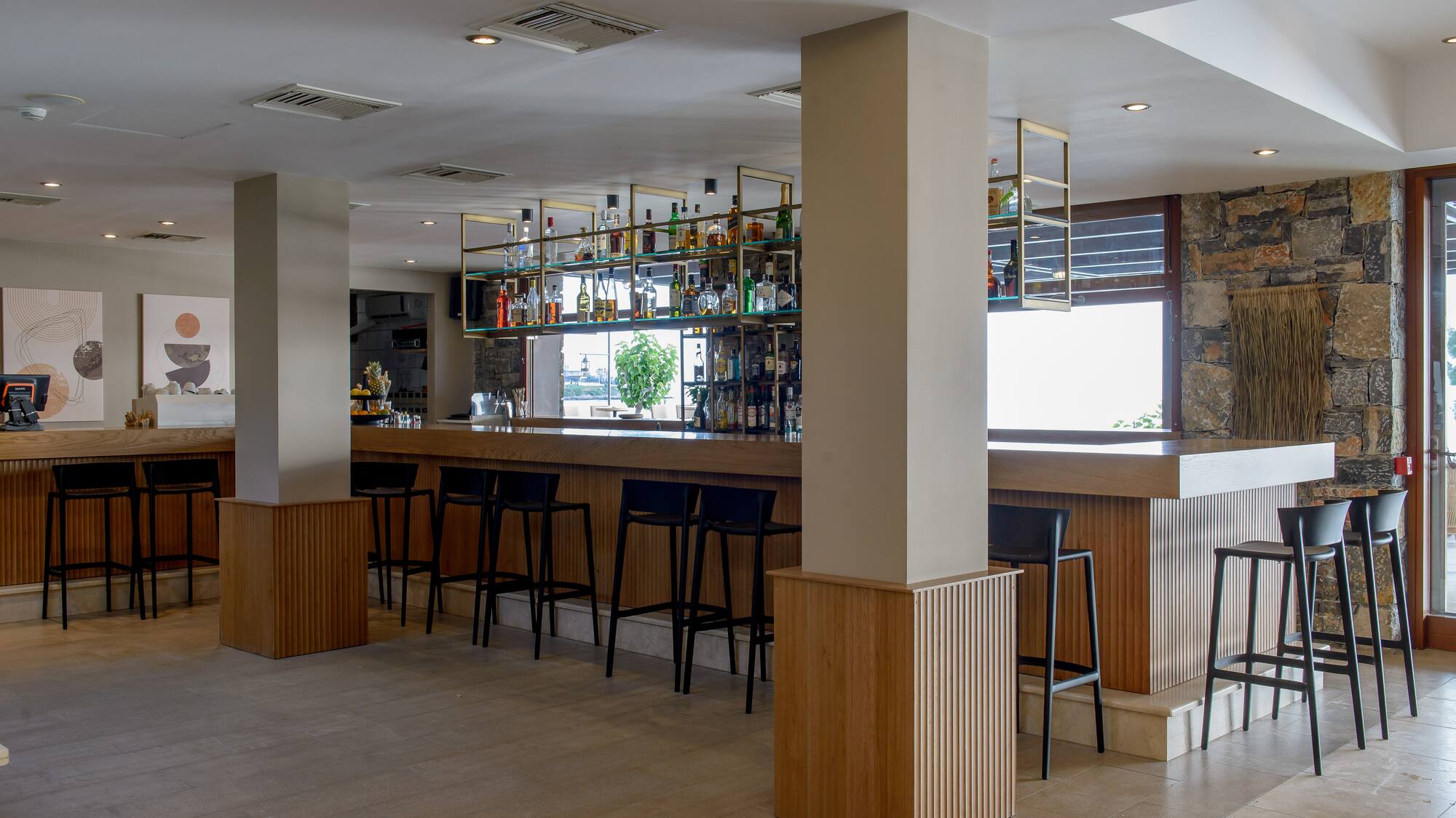 Modern hotel bar with wooden counter, black stools, and liquor display.