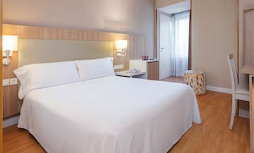 a bed with white sheets and a stool in a room