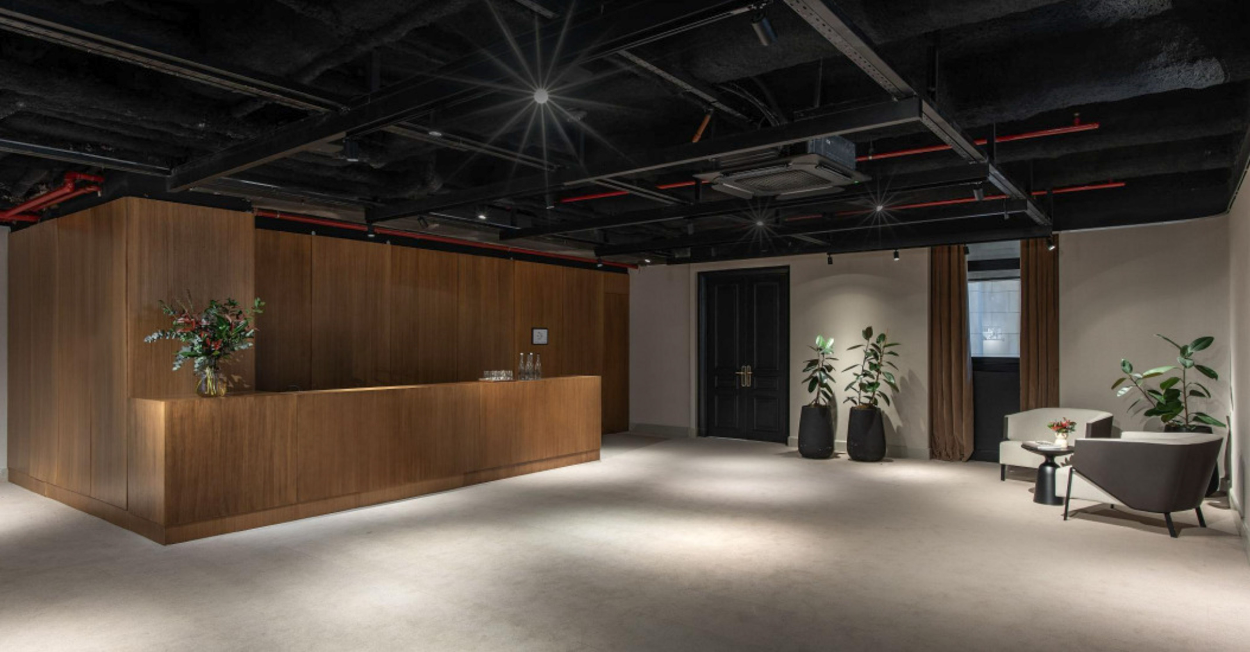 Modern office reception with wooden desk, exposed ceiling, and lounge area.