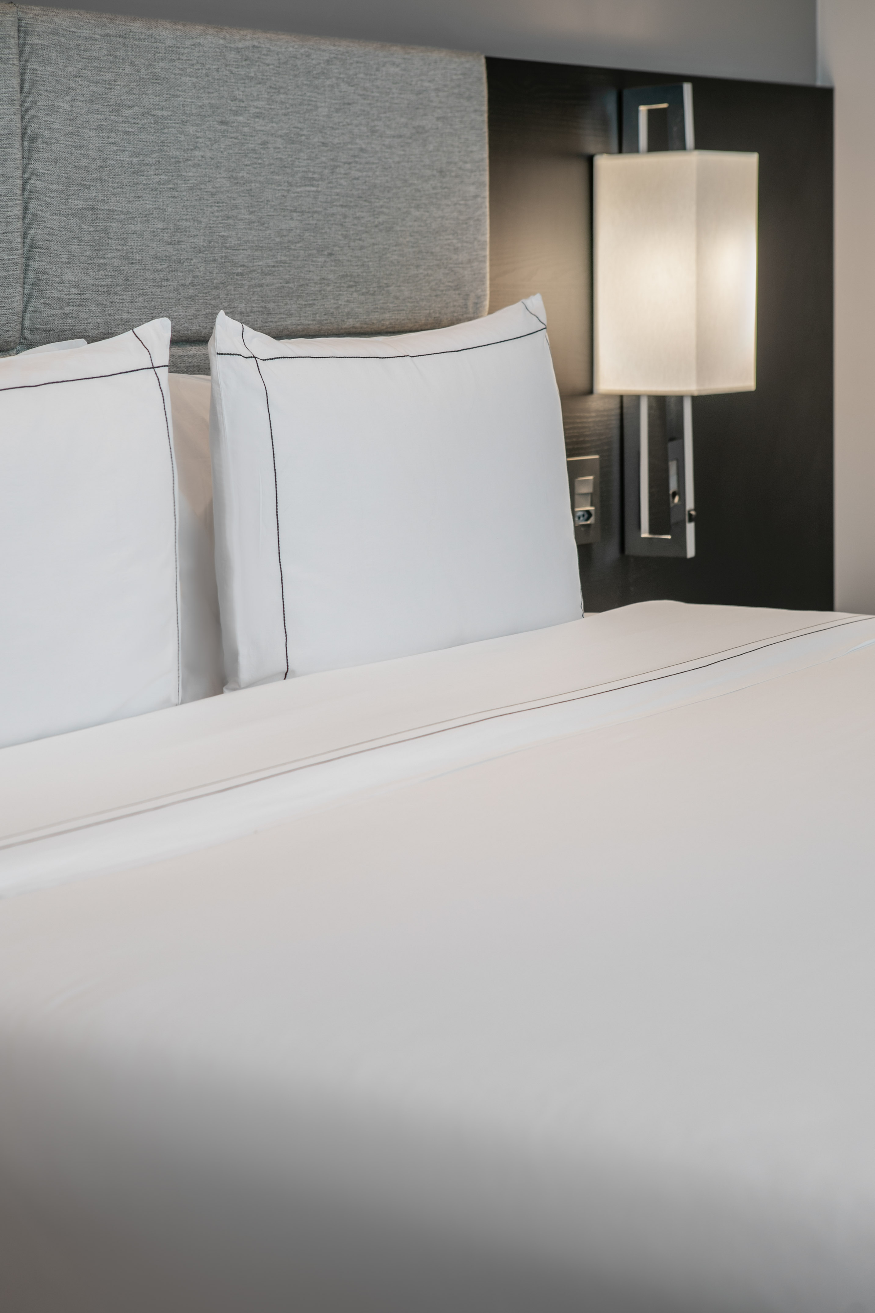 Hotel bed with white pillows, gray headboard, and modern wall sconce.