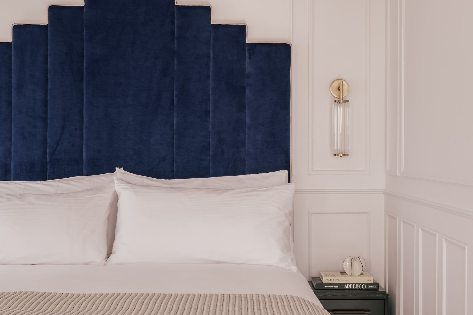 Luxury bedroom with blue velvet headboard, white bedding, and straw hat.