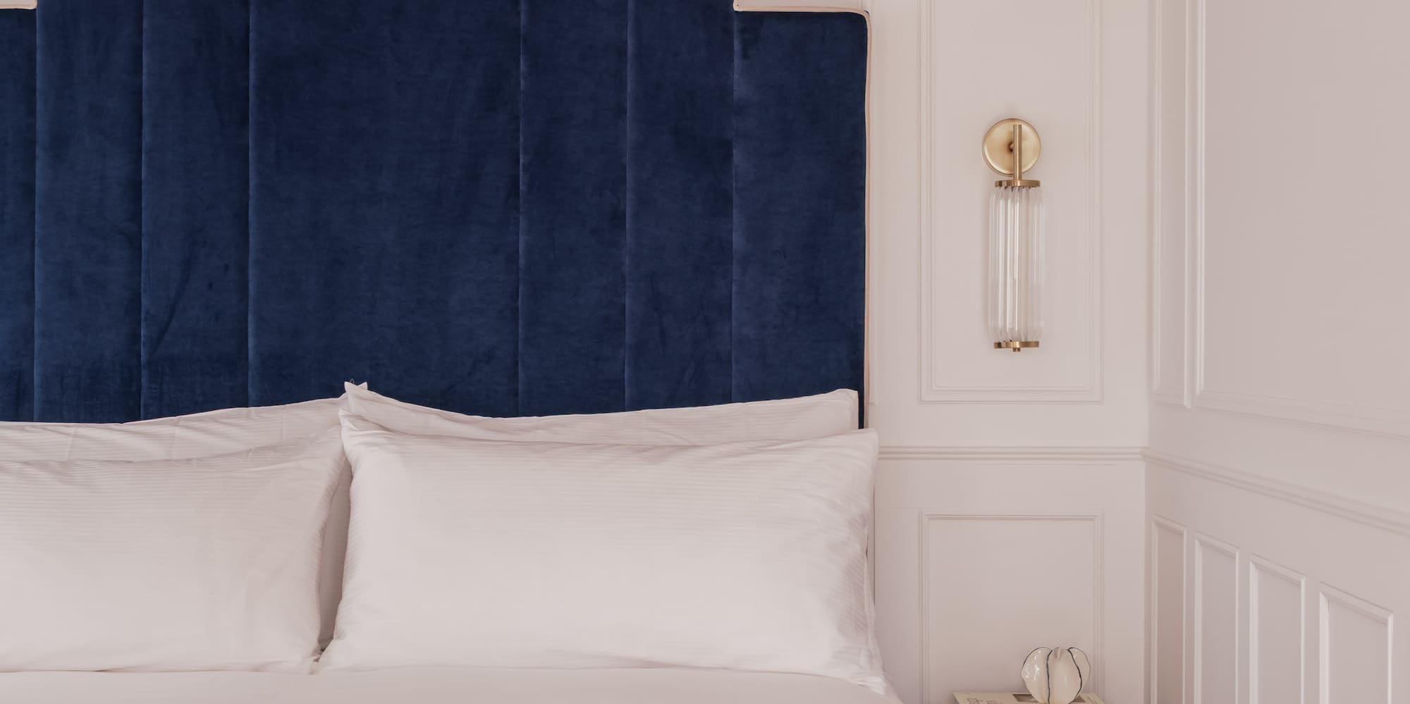 Blue velvet geometric headboard, white bed, striped blanket, nightstand in bedroom.